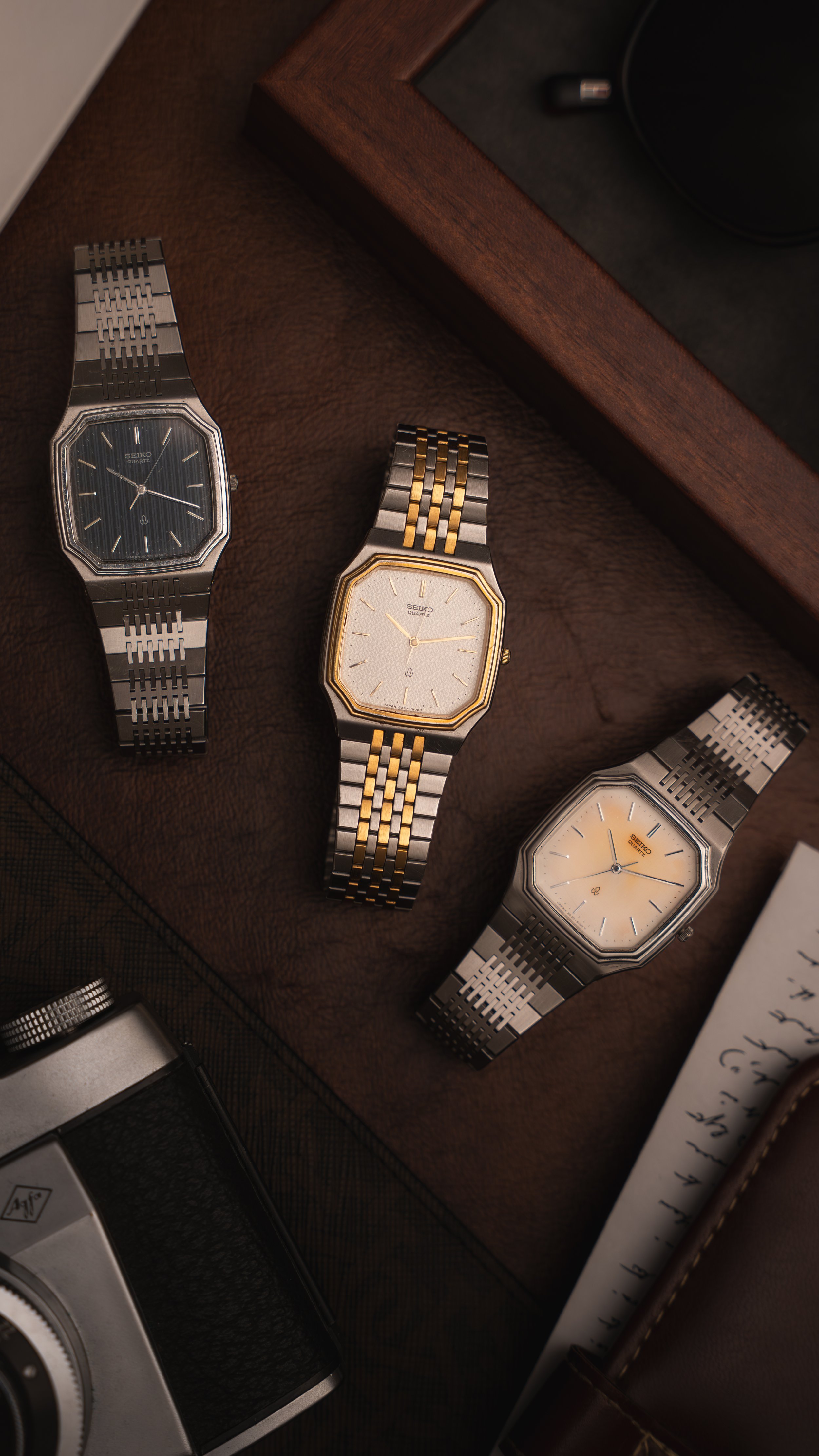 Collection of six vintage-style Seiko watches with metallic bands, displayed on a brown, silky fabric background, promoting their release date on October 3, 2025, and the drop date of October 8, 2025, titled "Midnight Steel," available for purchase at TimelessCuration.com.