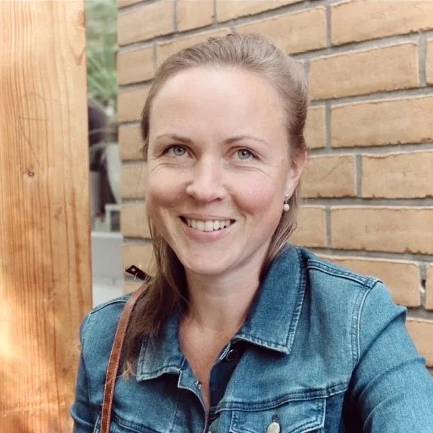 Lächelnde Frau mit braunen Haaren in Jeansjacke vor einer Ziegelwand