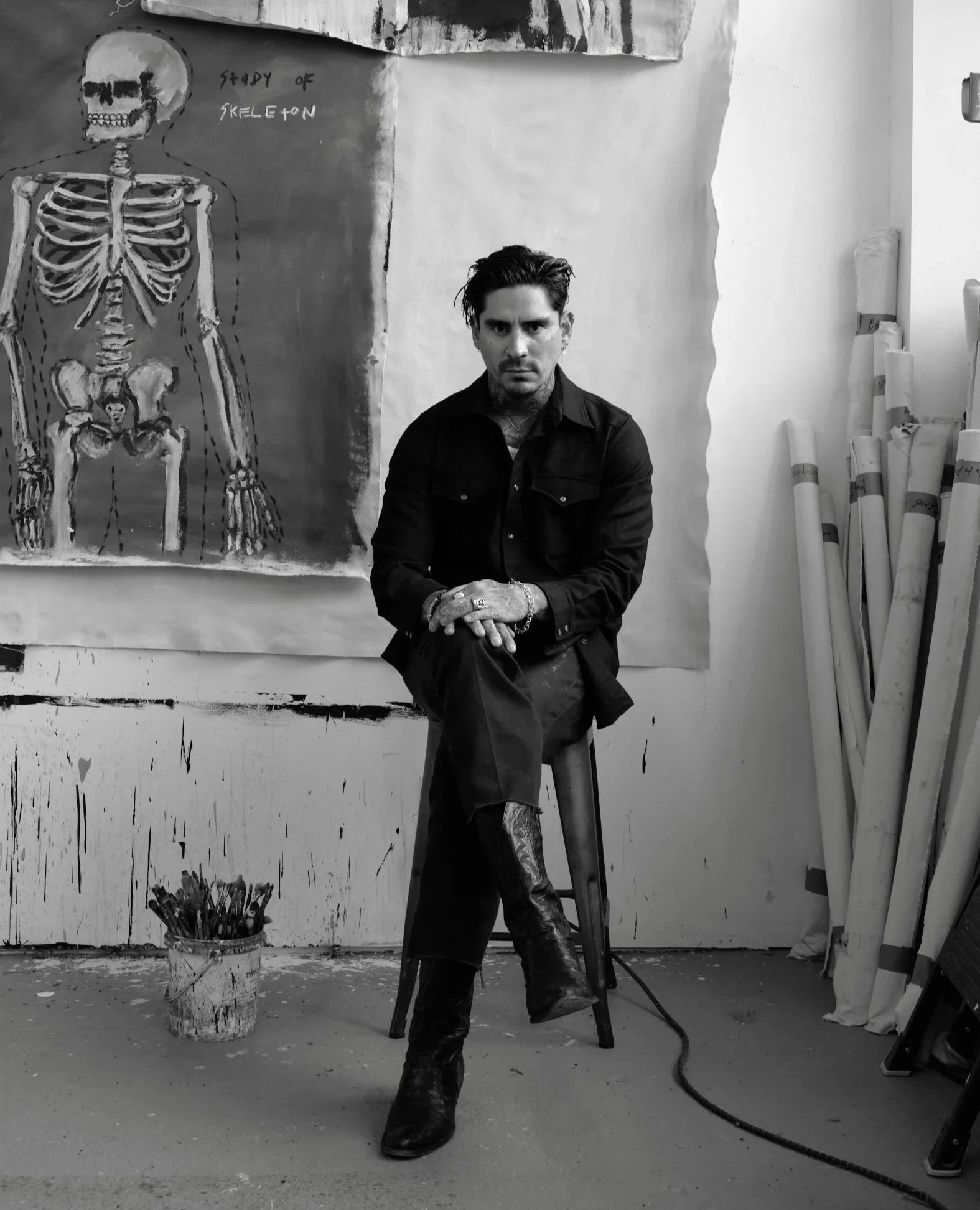 Black and white photograph of man sitting on a stool in his art studio