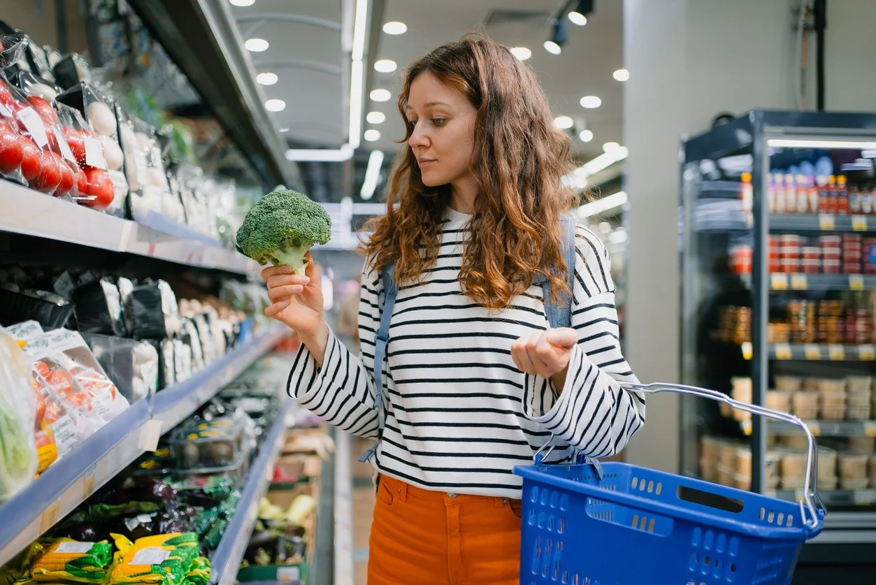 Woman shopping for broccoli in a grocery store aisle