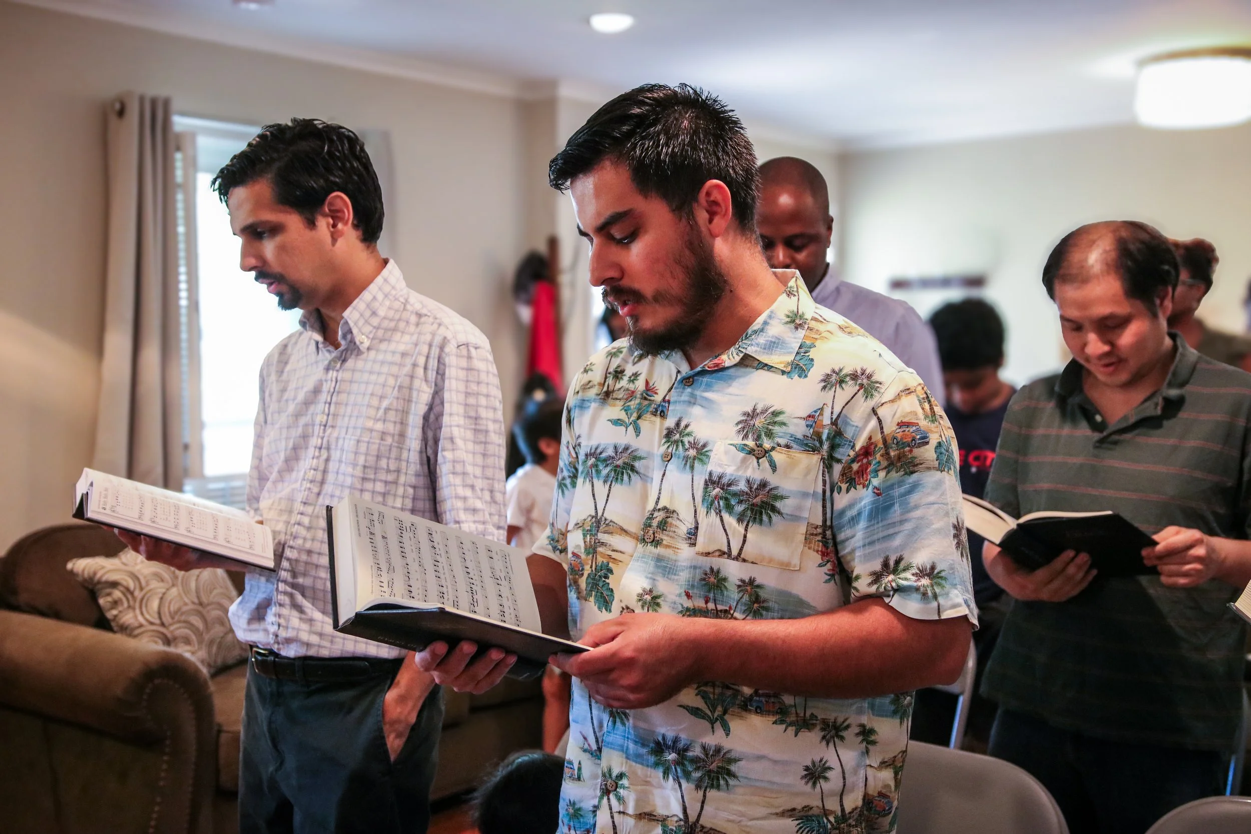 Group of men standing indoors, reading from books or hymnals, during a worship service.