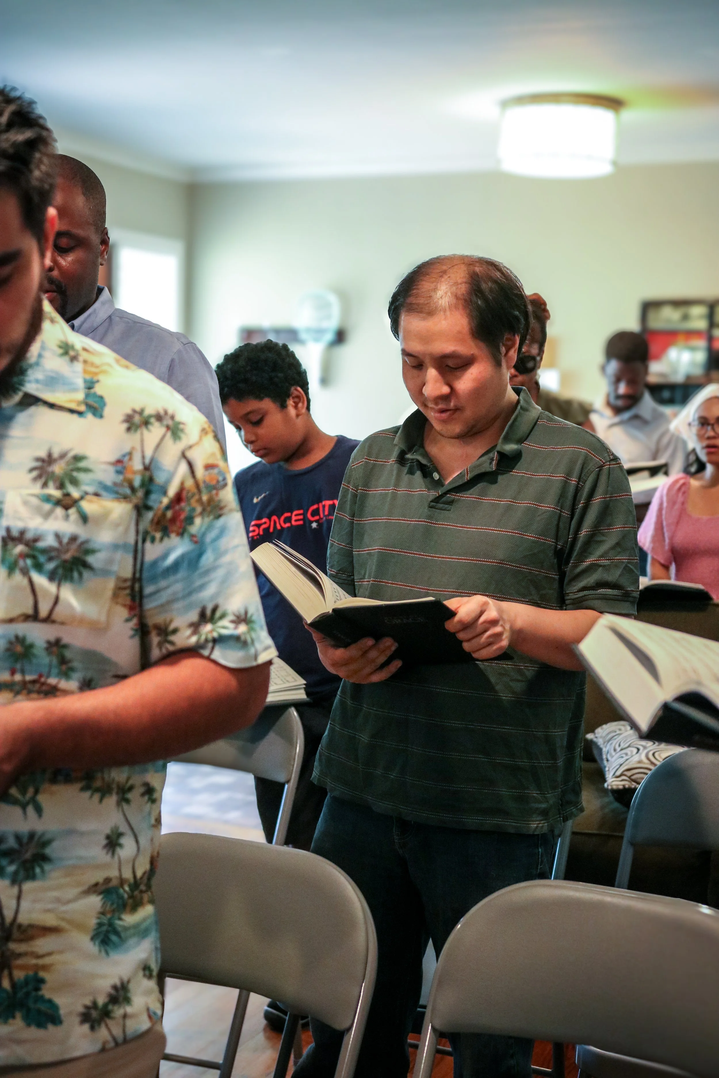 A group of people standing in a room, reading or holding books, during a worship service.