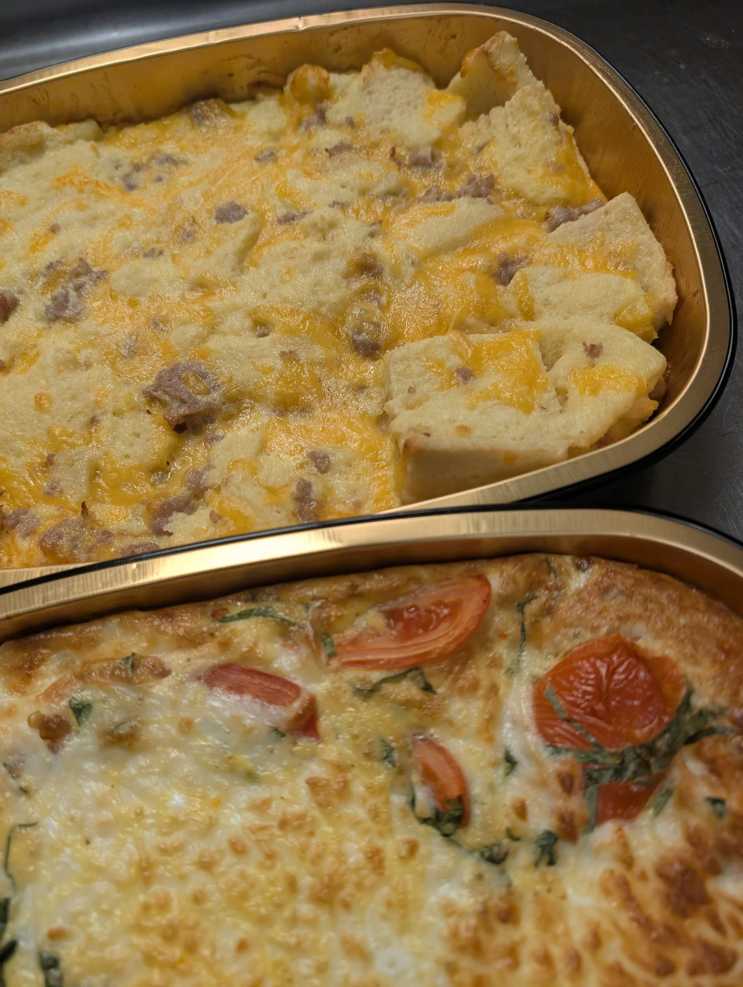 Two pans of cooked baked dishes, one containing cheesy breakfast casserole with sausage and cheese, the other containing an egg and cheese casserole with tomato slices and fresh basil.