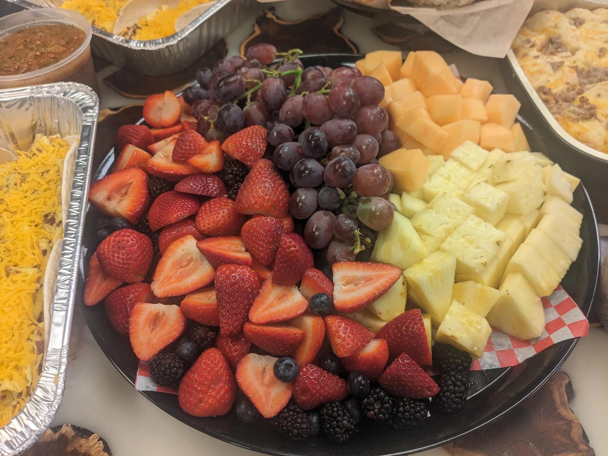 A platter of various cut fresh fruits, including strawberries, grapes, honeydew melon, pineapple, and cantaloupe.