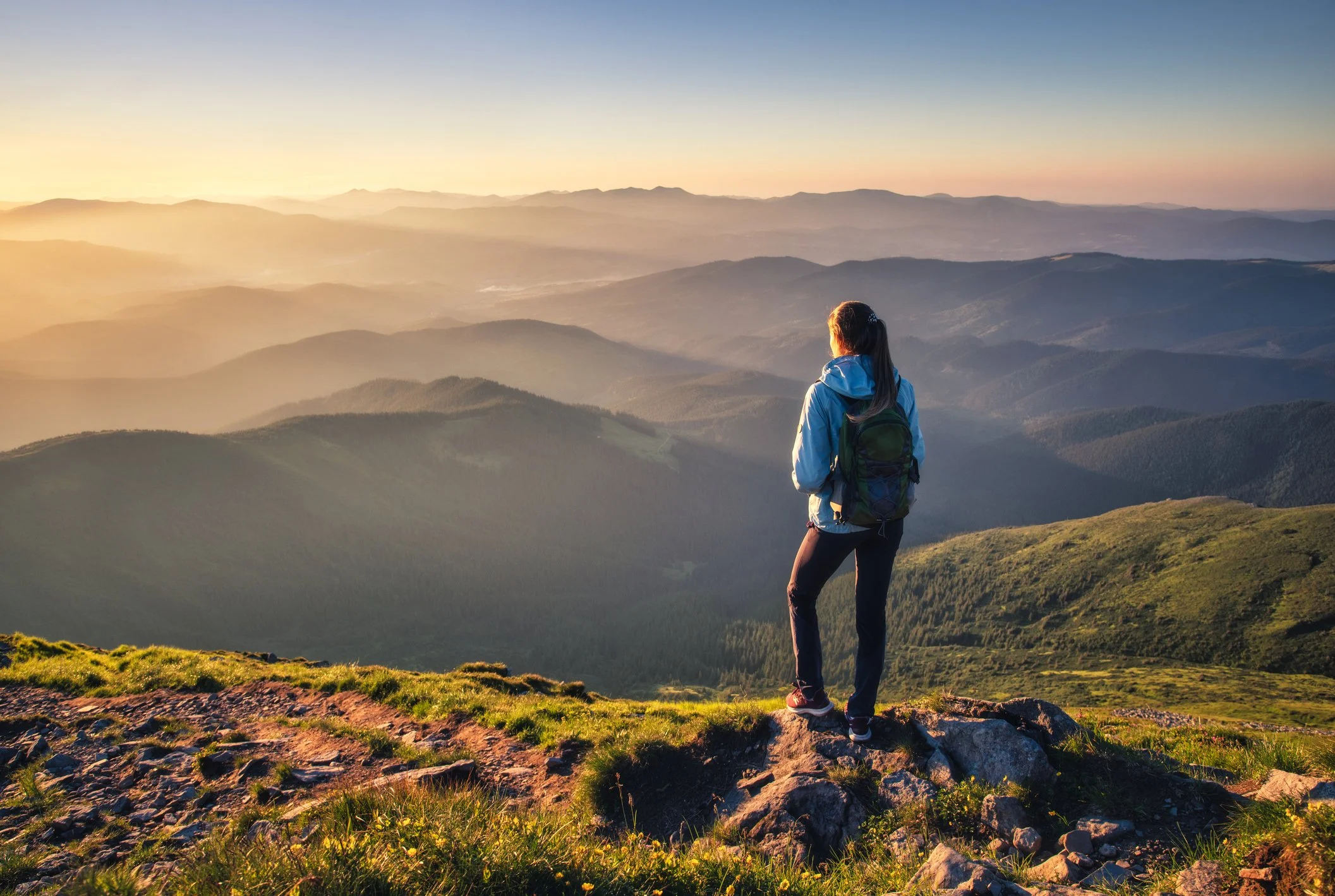Woman standing on a mountaintop at sunrise, mind-body healing for women breaking generational cycles