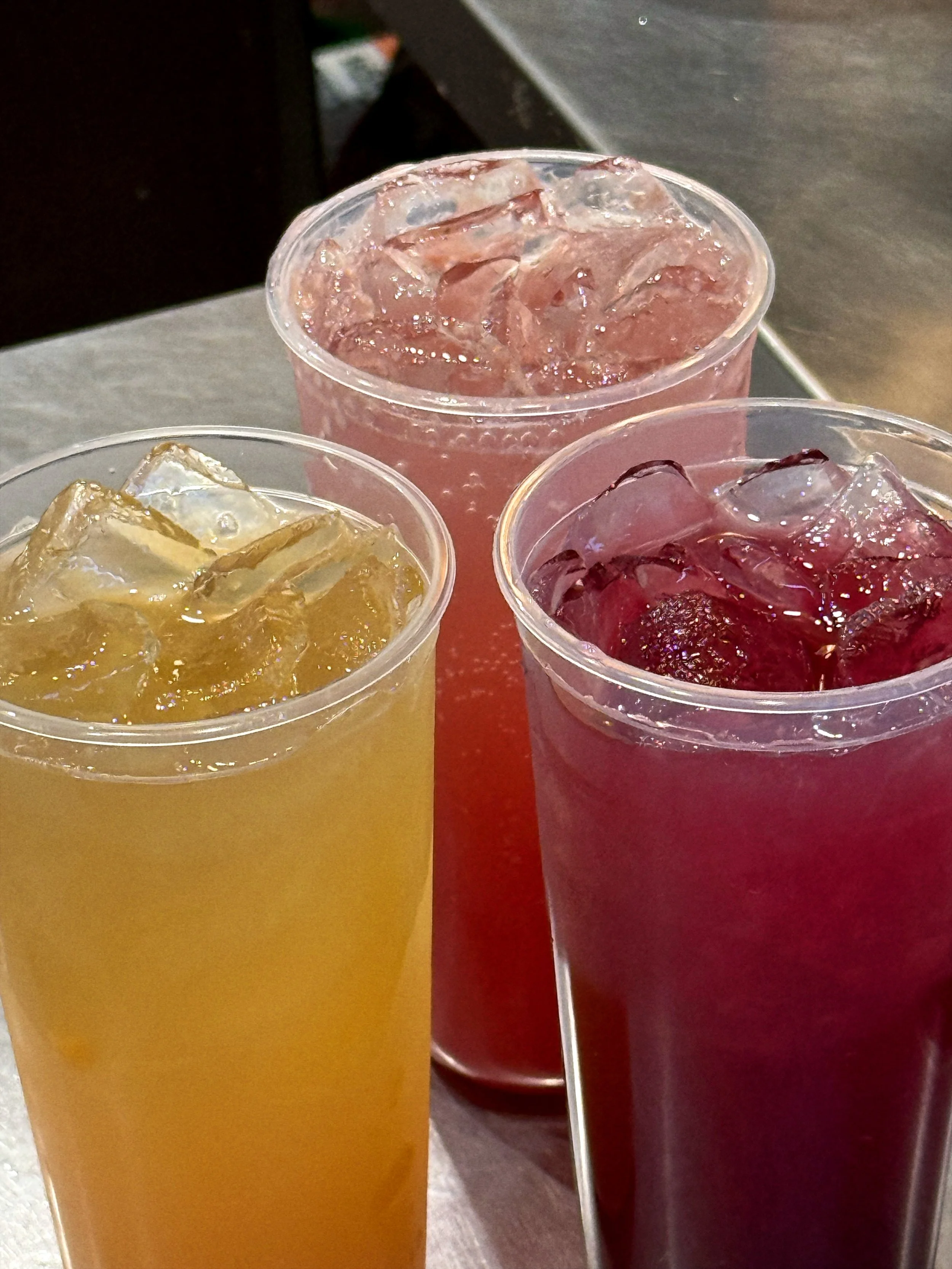 Three tall glasses filled with colorful iced beverages on a table.