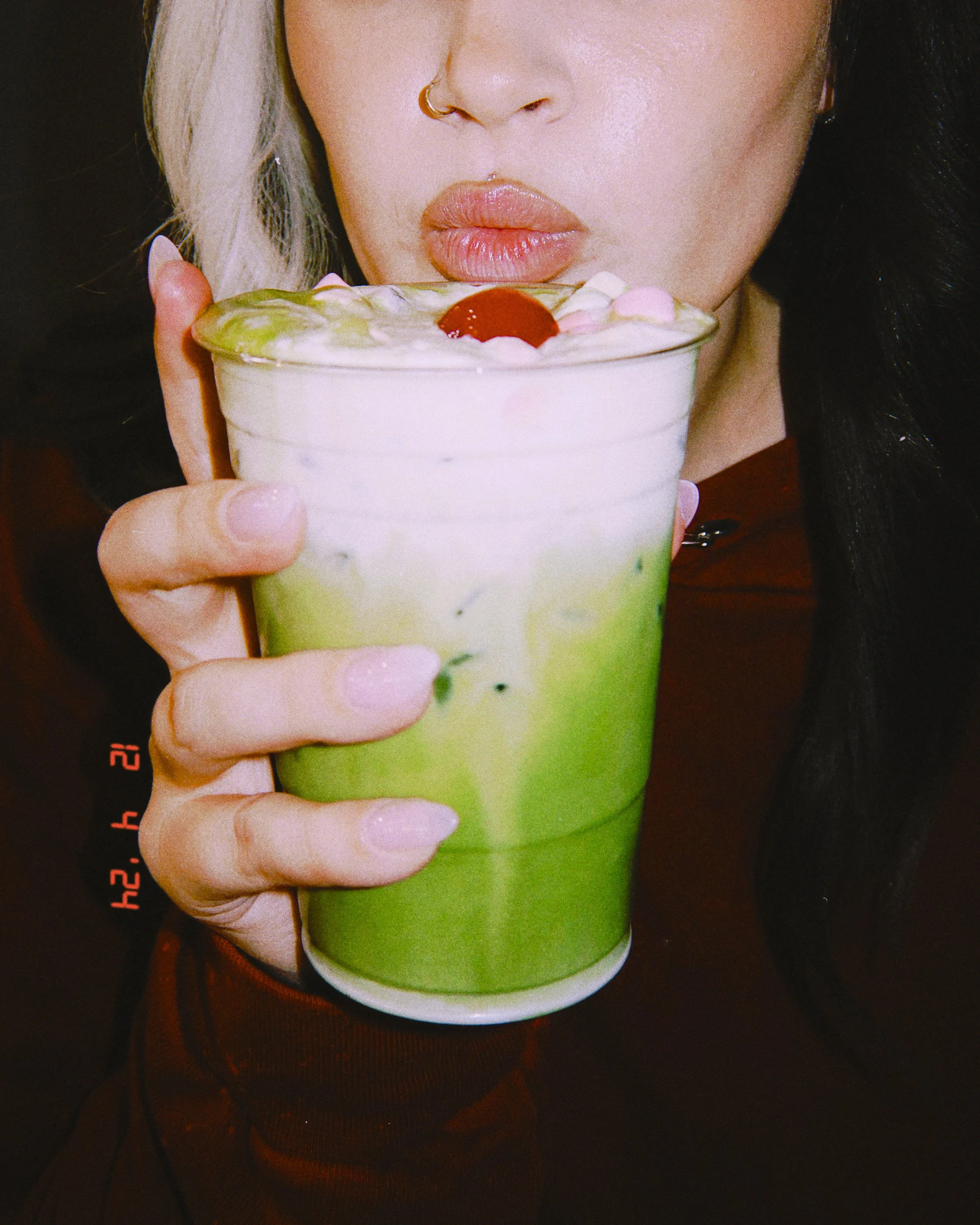 A woman holding a large green beverage topped with whipped cream and a cherry, with lips pursed near the drink.
