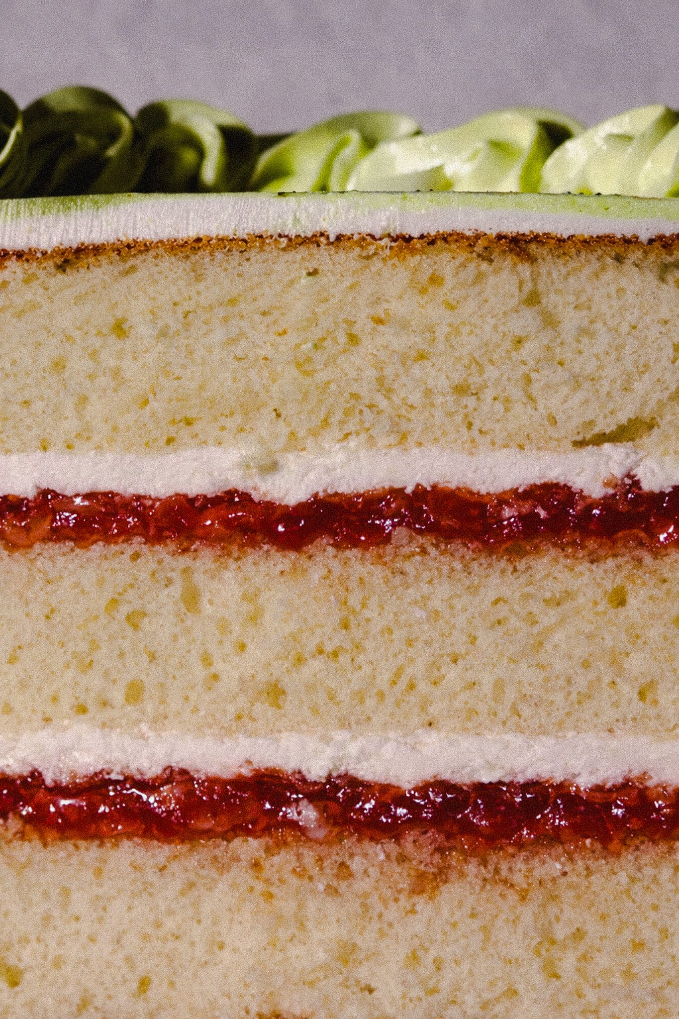 Close-up of a layered cake with white sponge and strawberry jam filling, topped with white frosting and green decorative curls.