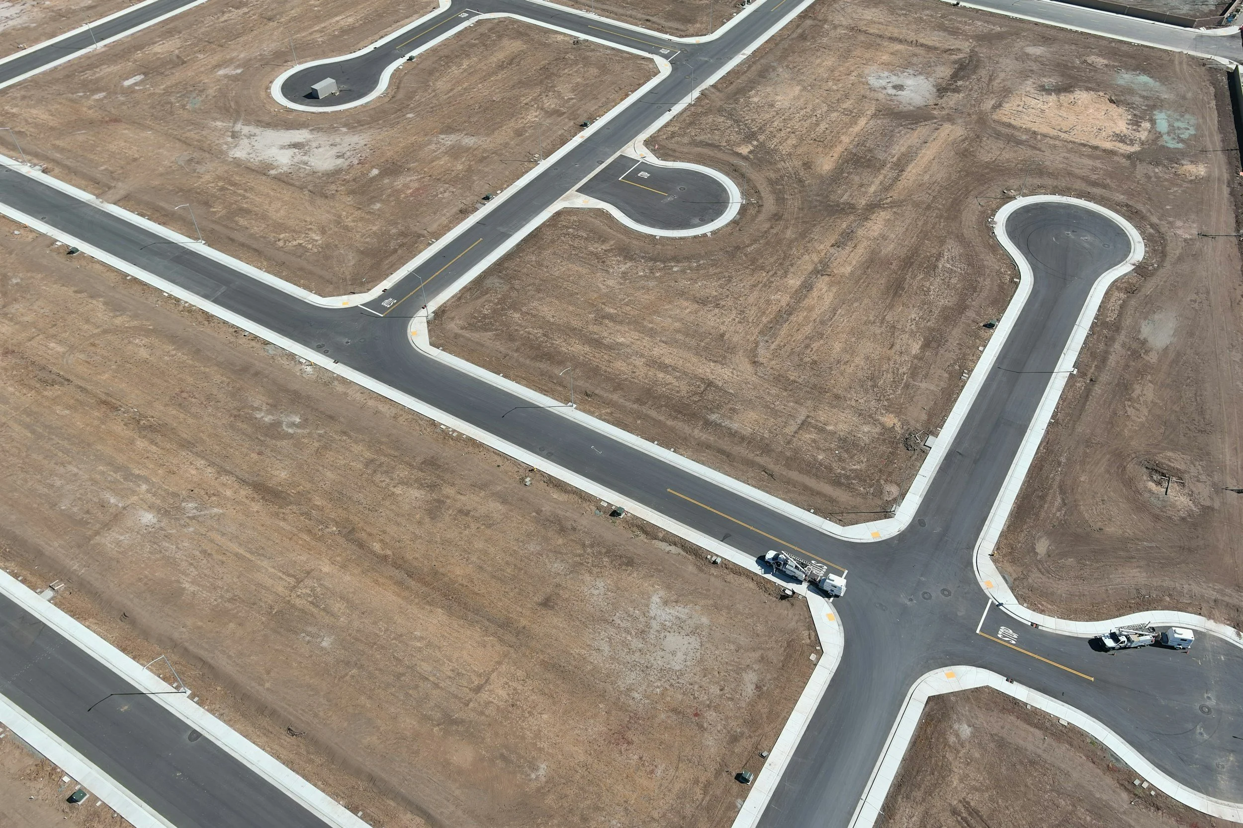 Aerial view of a construction site with newly paved roads and empty plots prepared for buildings.