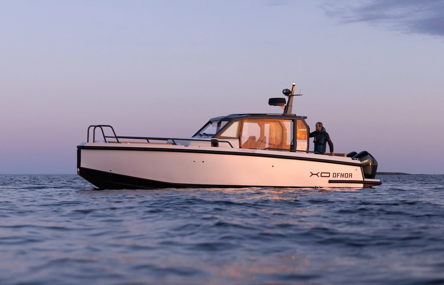 A white motorboat on the water during sunset with a man standing onboard, a clear sky, and calm water.