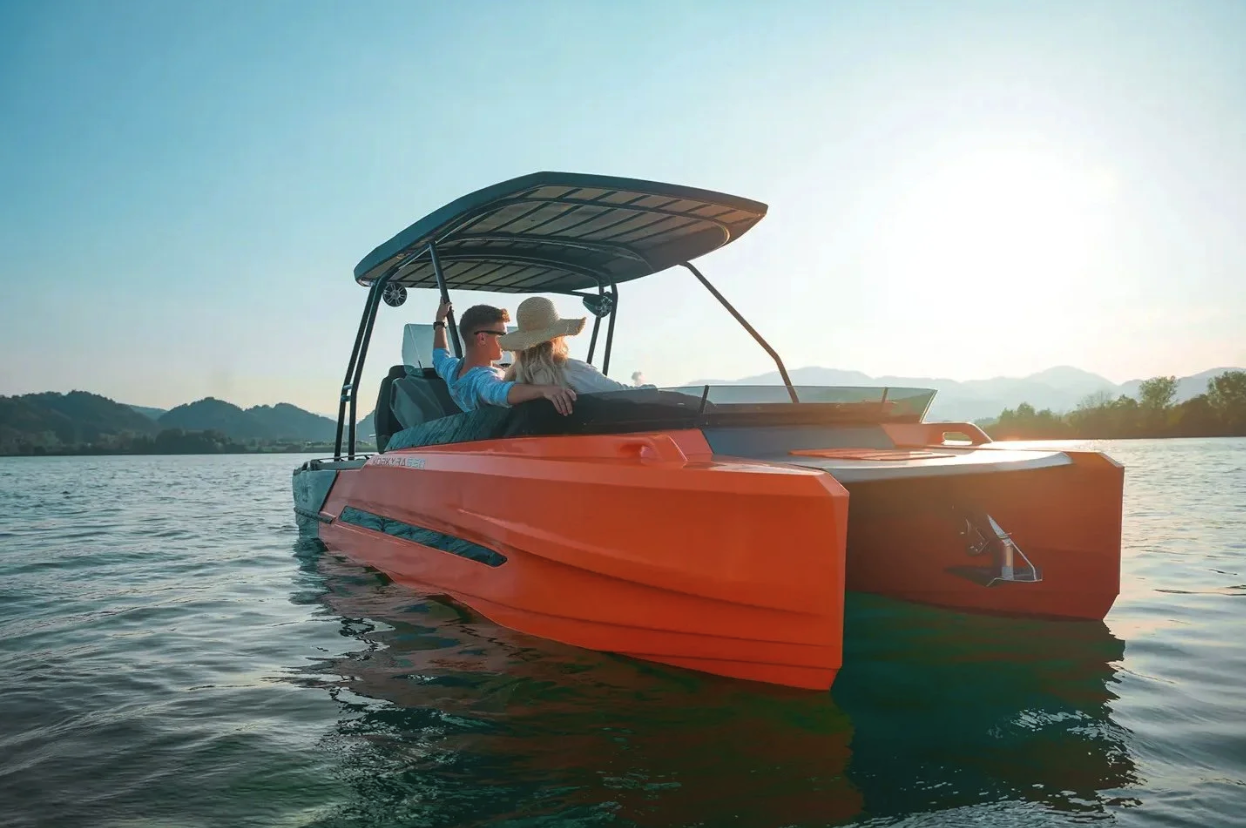 A couple on a bright orange boat on a lake during sunset, with mountains in the background.