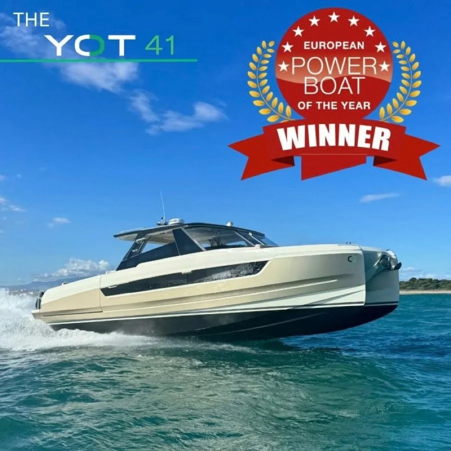 A large modern powerboat speeding through the water under a blue sky with some clouds, awarded the European Power Boat of the Year and winner badge.