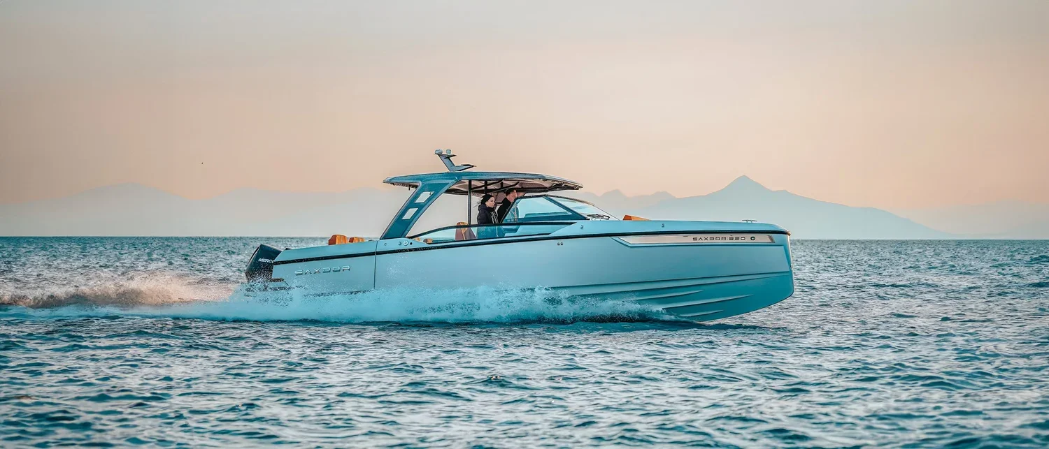 A modern blue yacht moving across the water with distant mountains and a clear sky in the background.