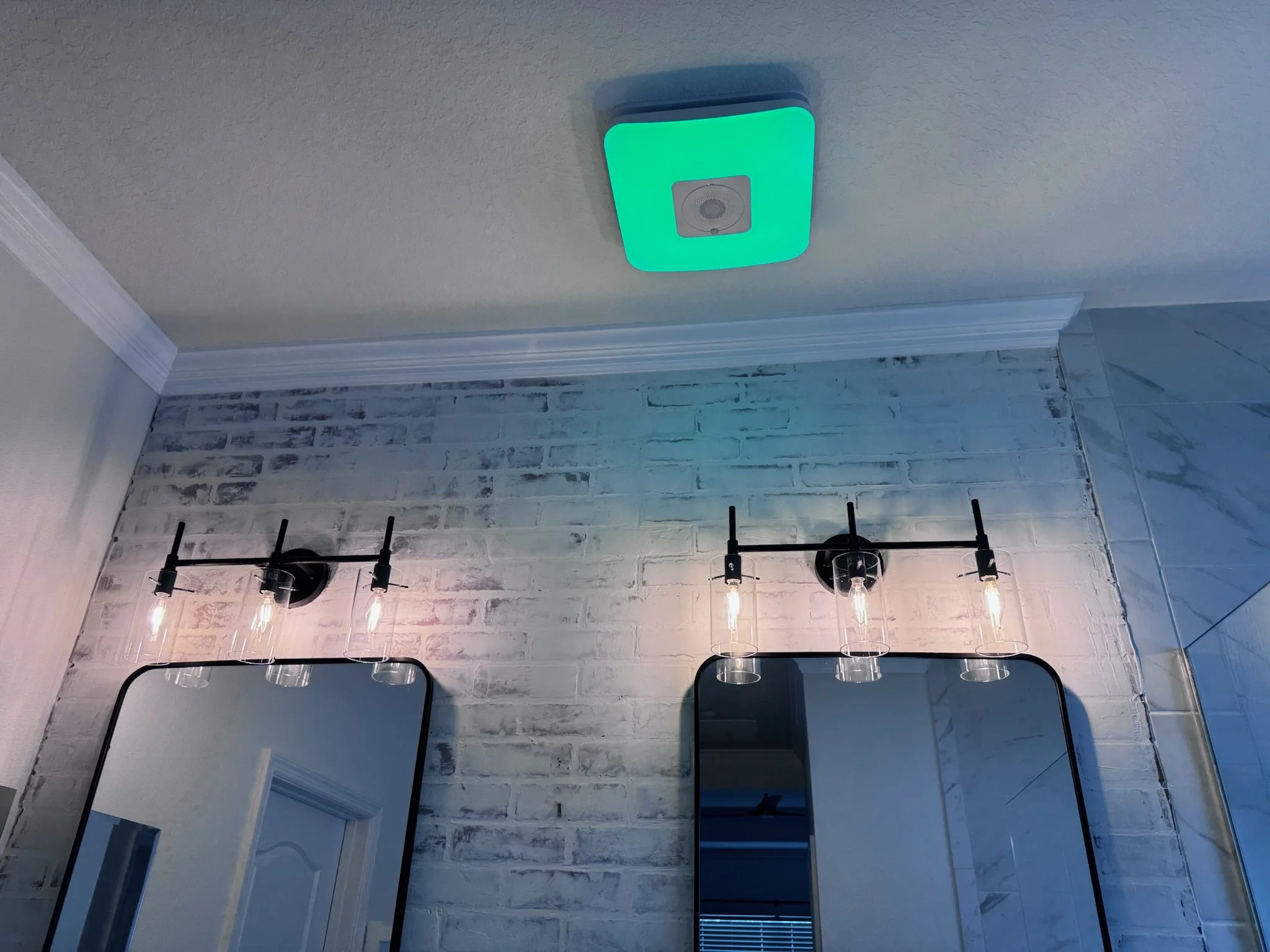 Ceiling-mounted square light fixture emitting green light, with a small speaker in the center, in a room with white textured ceiling and crown molding.