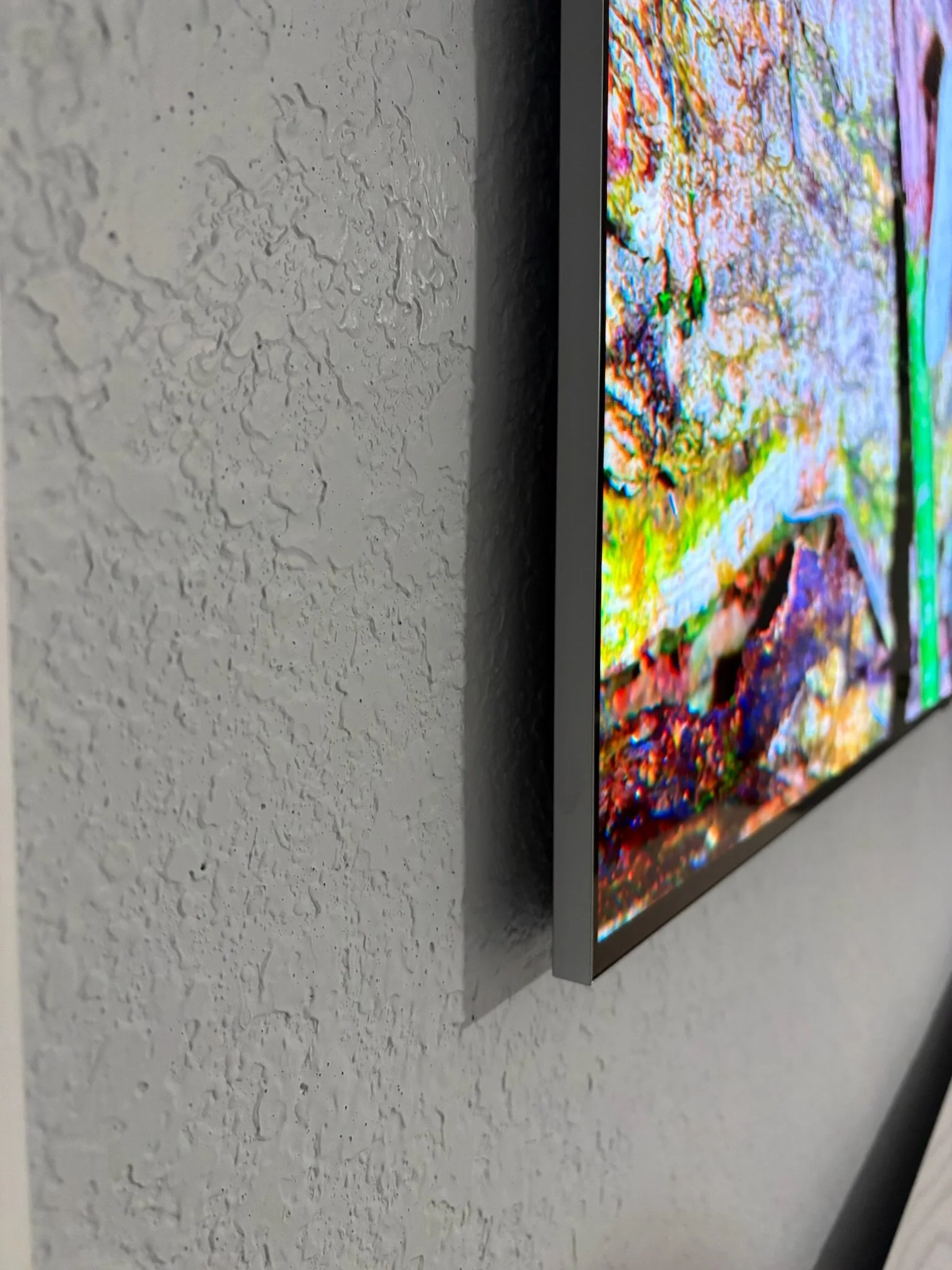 Close-up photo of a textured white wall with a colorful digital screen showing abstract art.