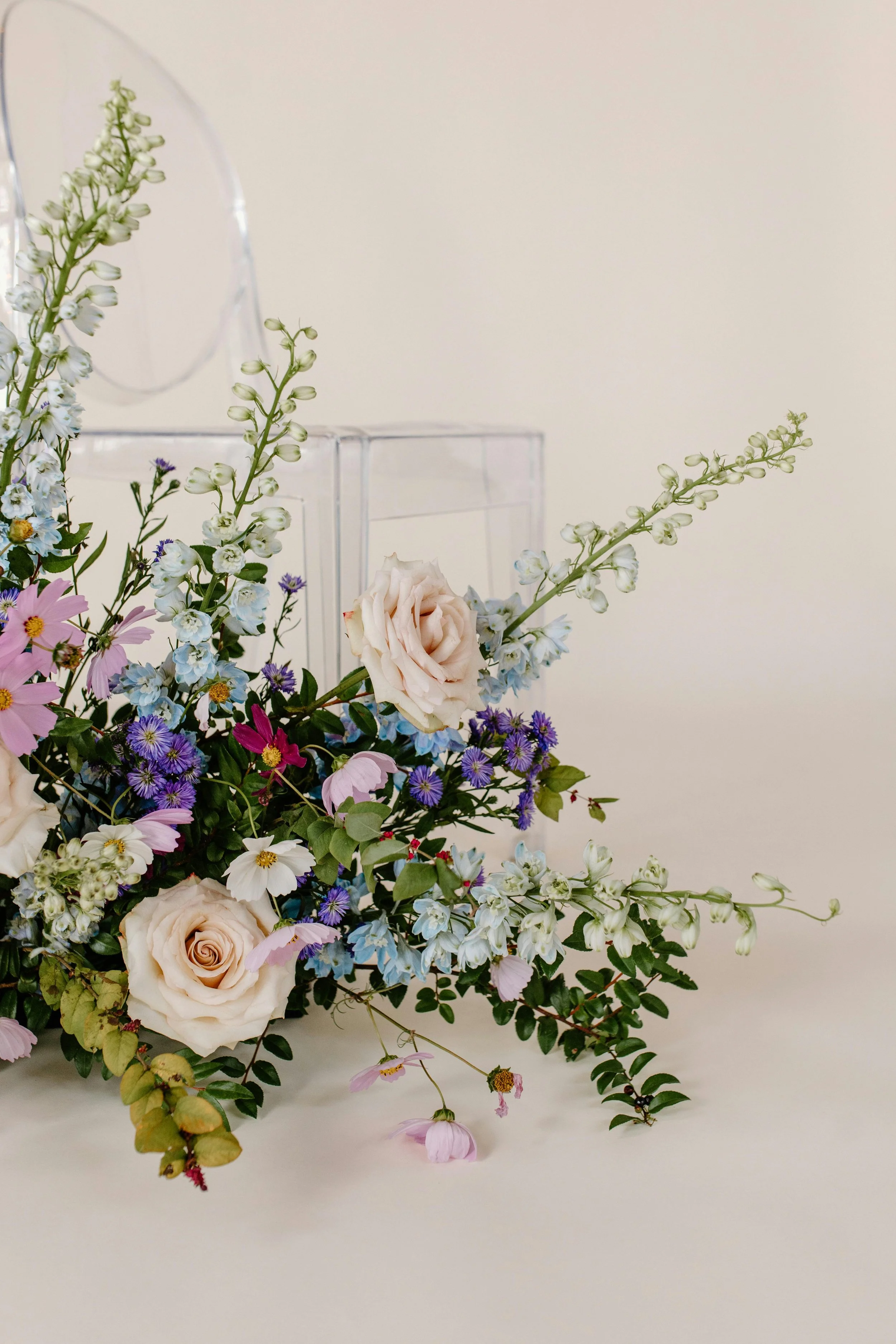 Arrangement of pink, white, purple, and blue flowers with greenery on a white surface against a light background.