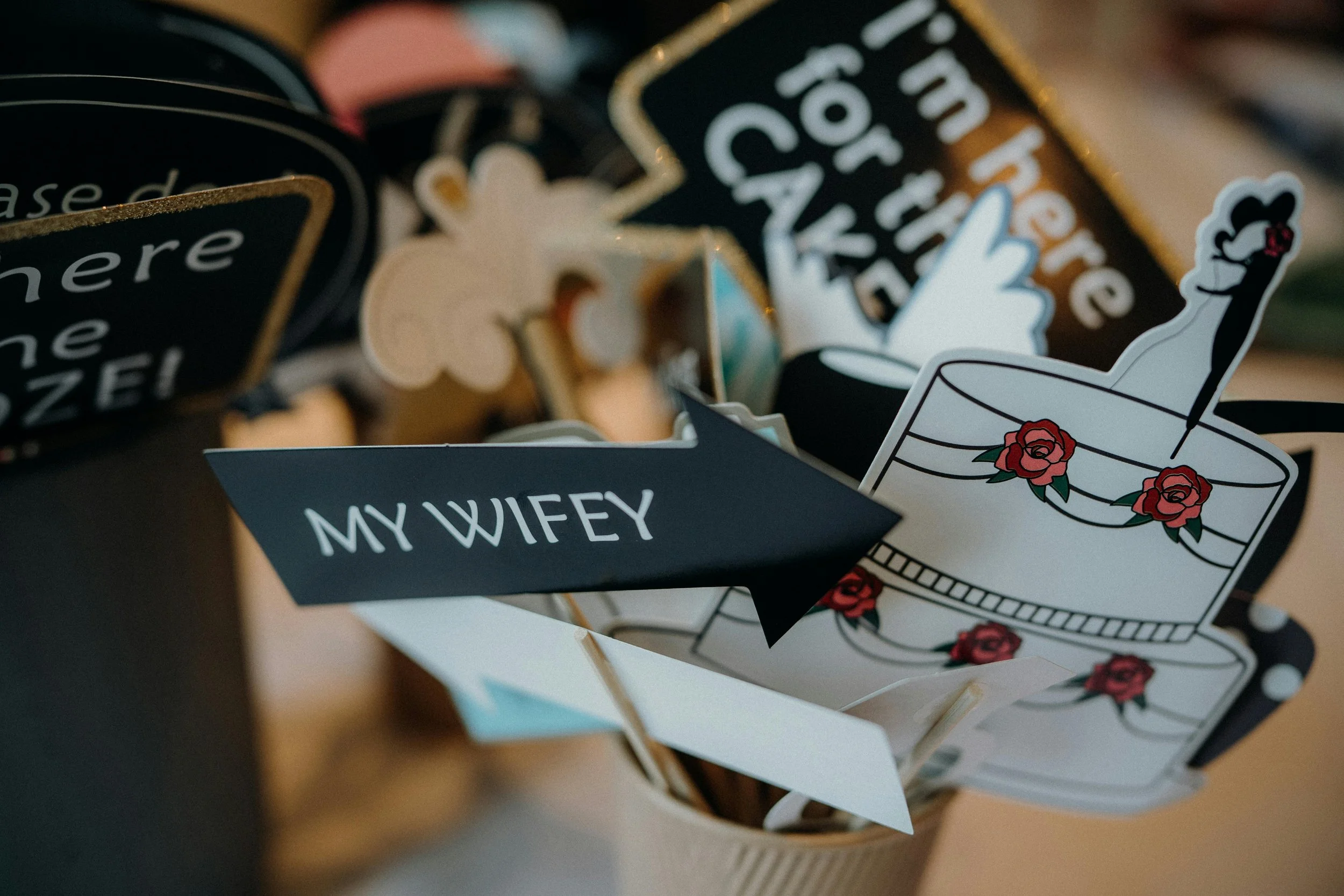 Decorative paper signs and cutouts, including a sign reading "MY WIFEY" pointing to a cake illustration, in a container likely for a celebration or party.