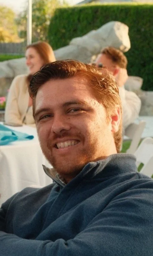 Zack Shetler, founder of Sandpiper Property Media, a young man with light skin and brown hair smiling outdoors, at a gathering near a grassy area with rocks.