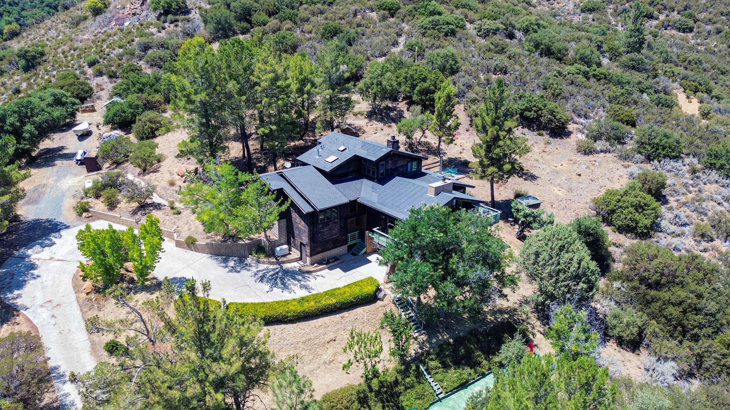 Aerial view of a large house surrounded by trees and dry landscape, with a driveway and outdoor area.