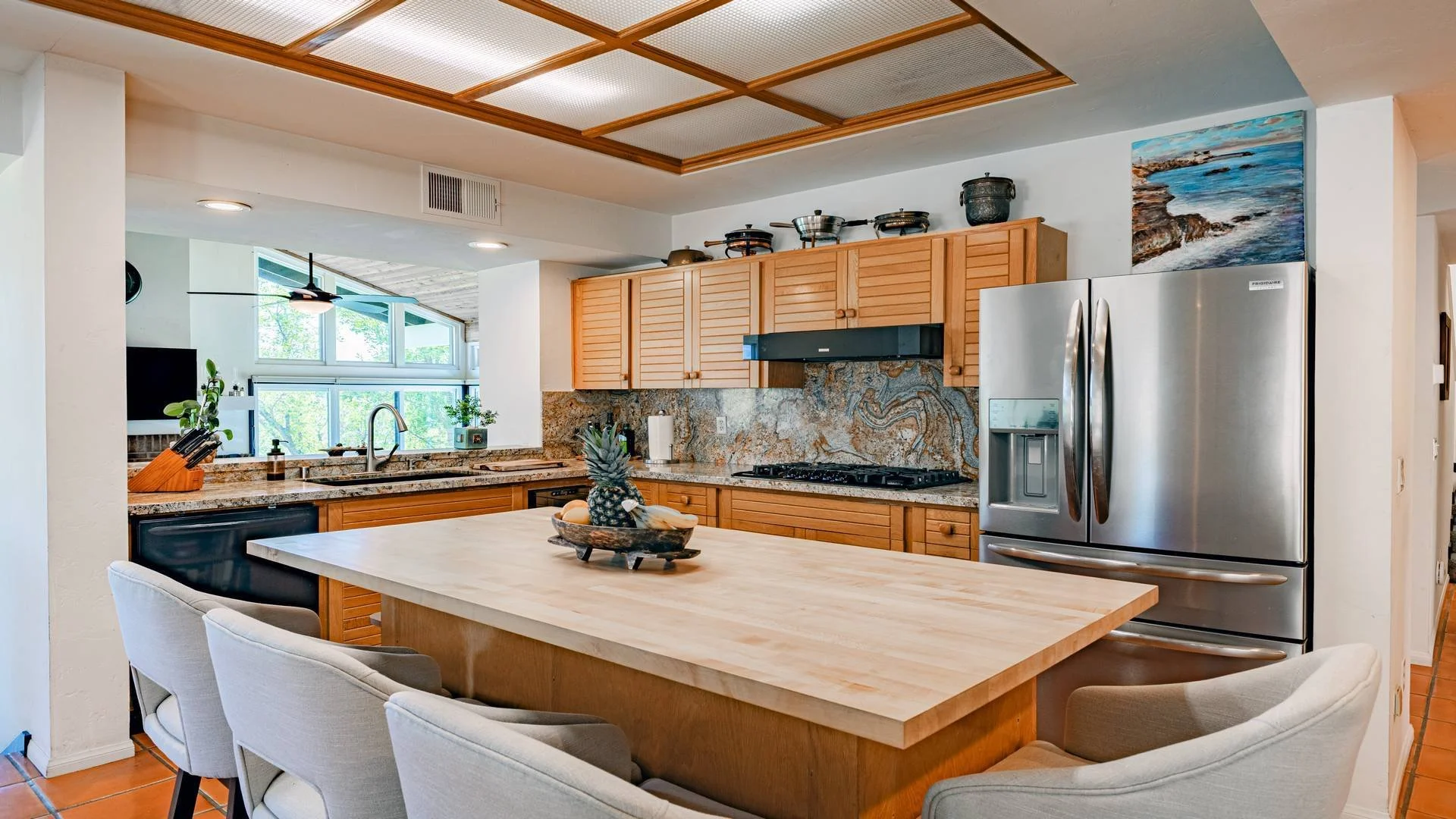 Single family home kitchen with wooden cabinets, granite countertops, stainless steel fridge, and a kitchen island with chairs. Interior photography of a come in East San Diego County. 