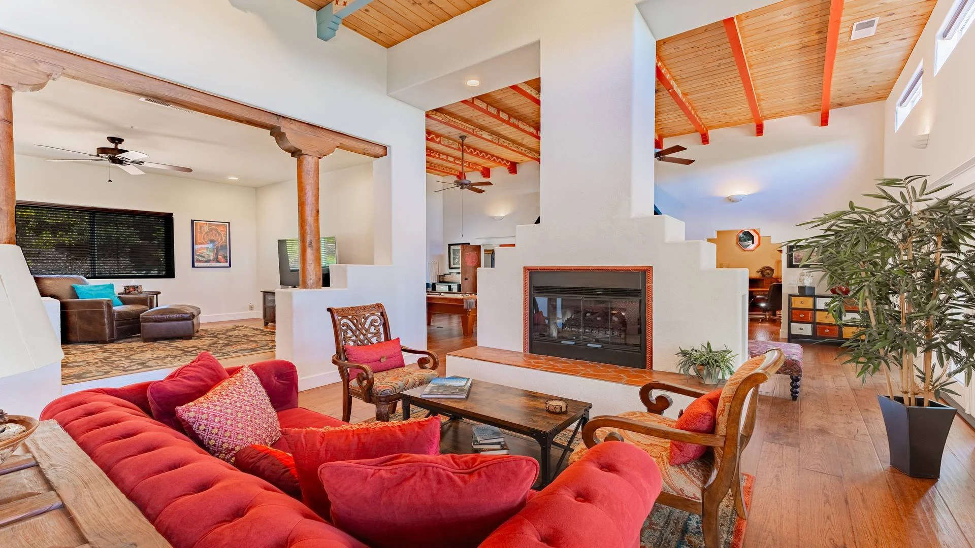 Living room with red sofa, wooden furniture, fireplace, plants, ceiling fans, and a mix of modern and rustic decor. Luxury real estate photography in Inland San Diego. 
