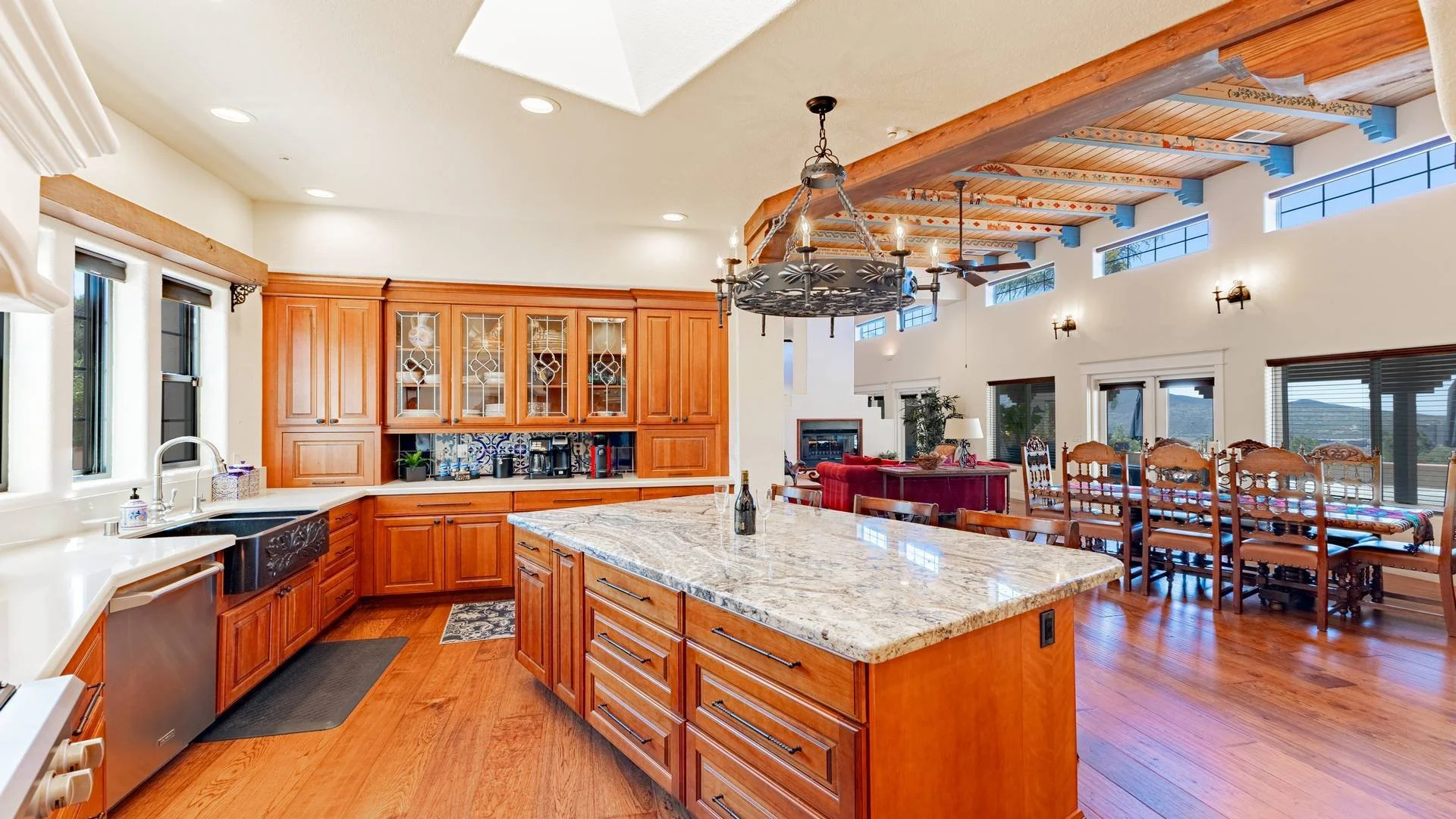 Spacious kitchen with wooden cabinets, granite island, and high ceilings with exposed beams, leading into a dining and living area with large windows and mountain views.