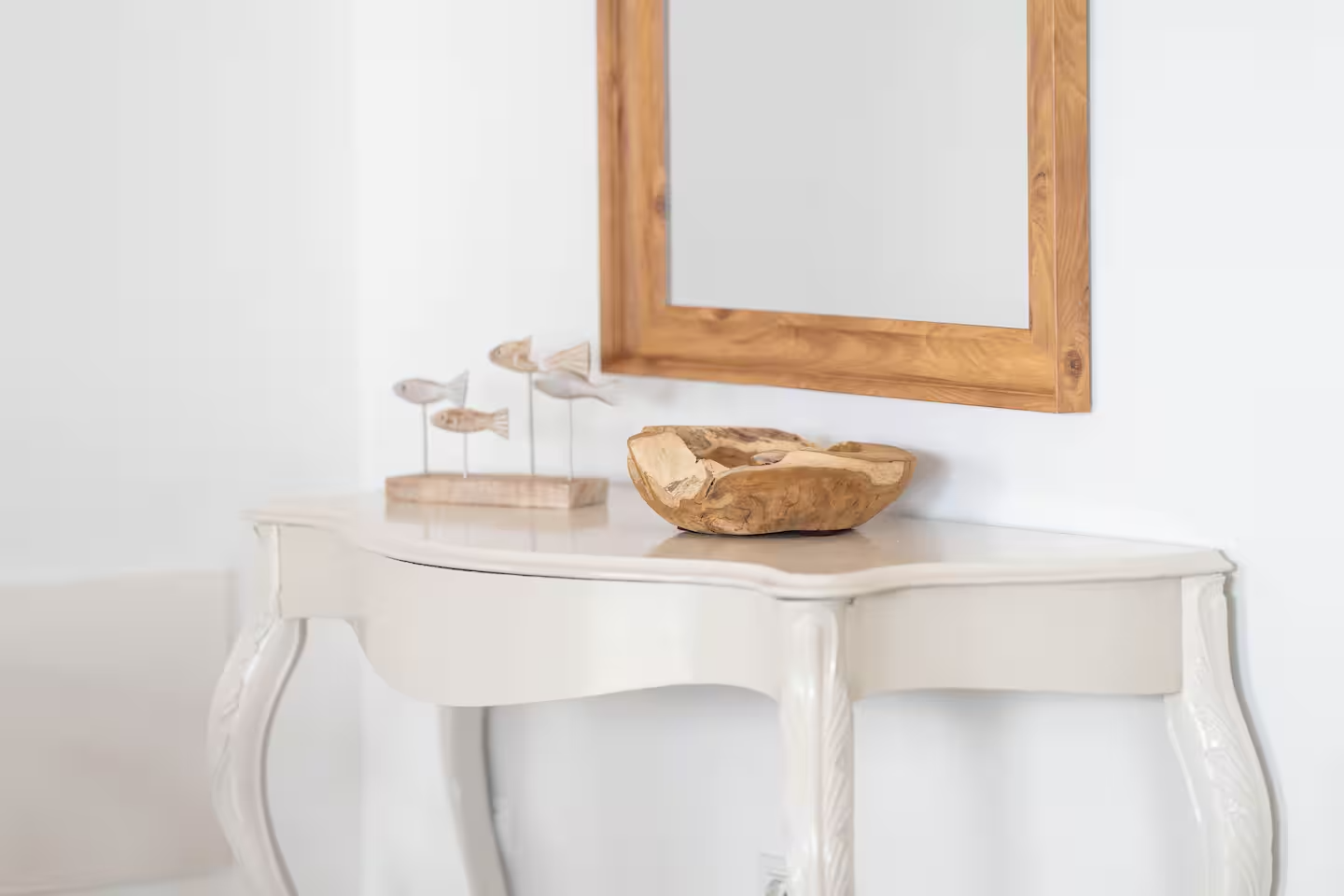 Espejo de madera sobre mesa blanca decorada con figura de peces y un recipiente de madera.