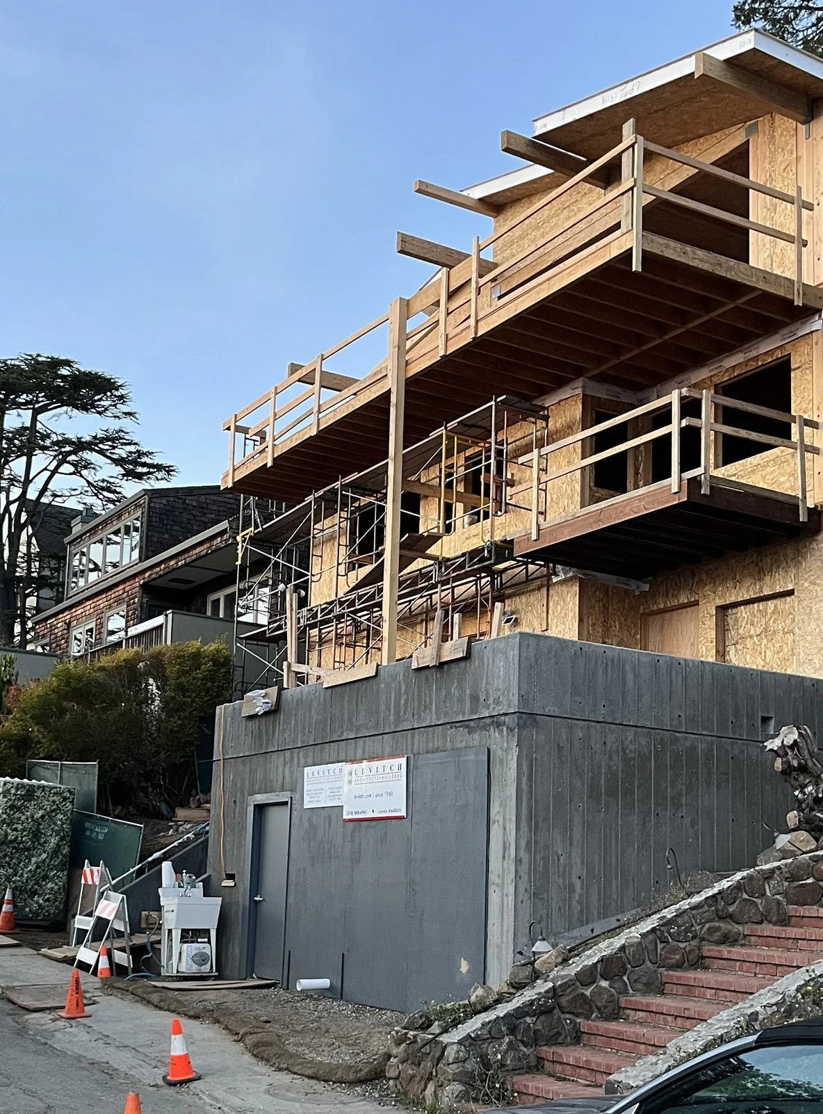 Street view of new 3 story home framed in SIPS. Garage at front stepping back to scaffolded front with multi-pitched roof
