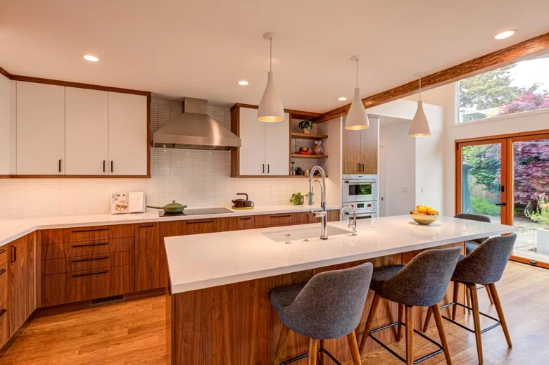 Kitchen island view showing custom walnut cabinets, integrated appliances, pendant lighting, and a generous workspace designed to maximize storage and functionality for a growing family.