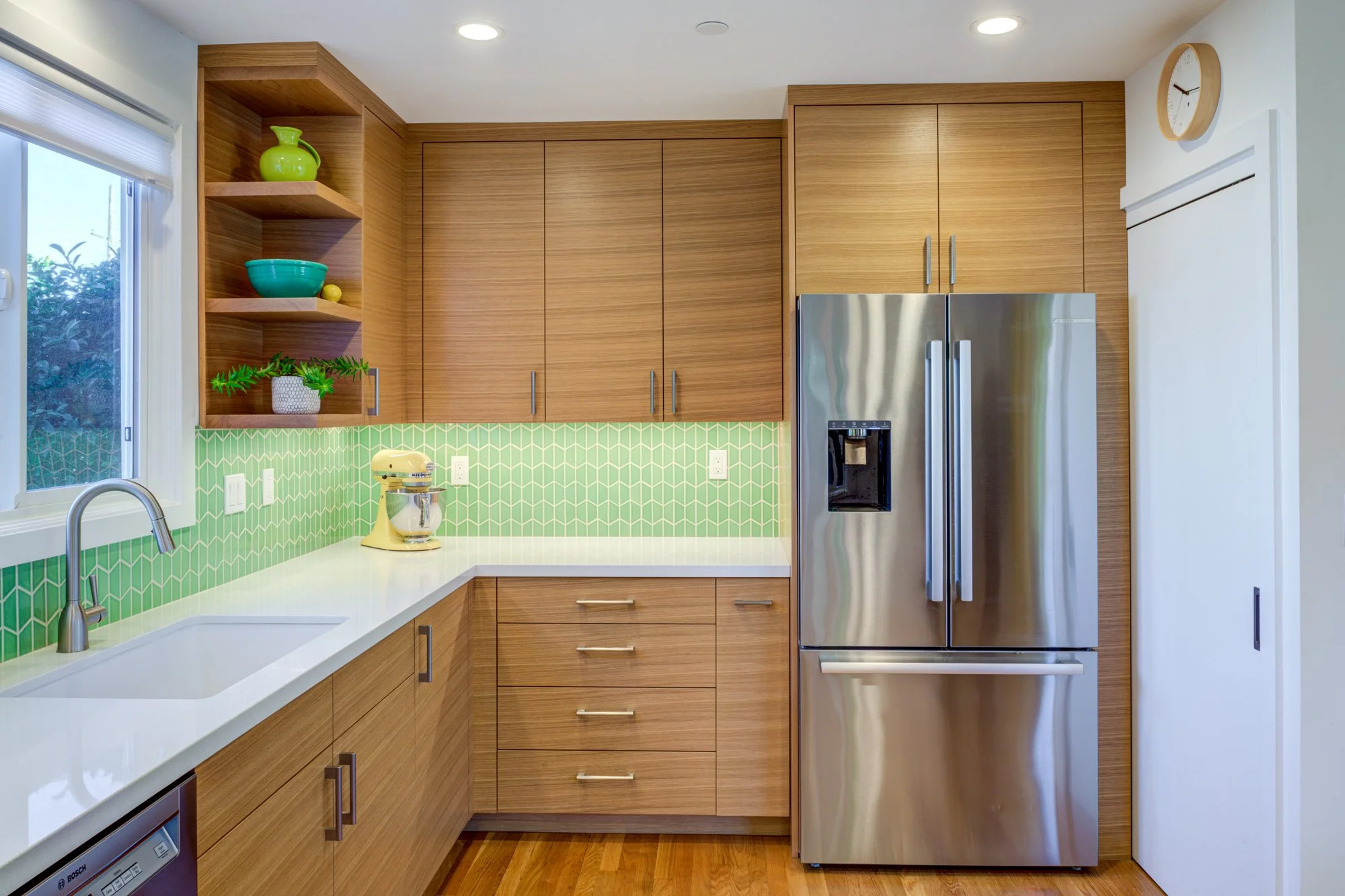 Kitchen view showing custom wood cabinetry, integrated pantry storage behind a flush door, and green tile backsplash designed for efficiency and visual continuity.