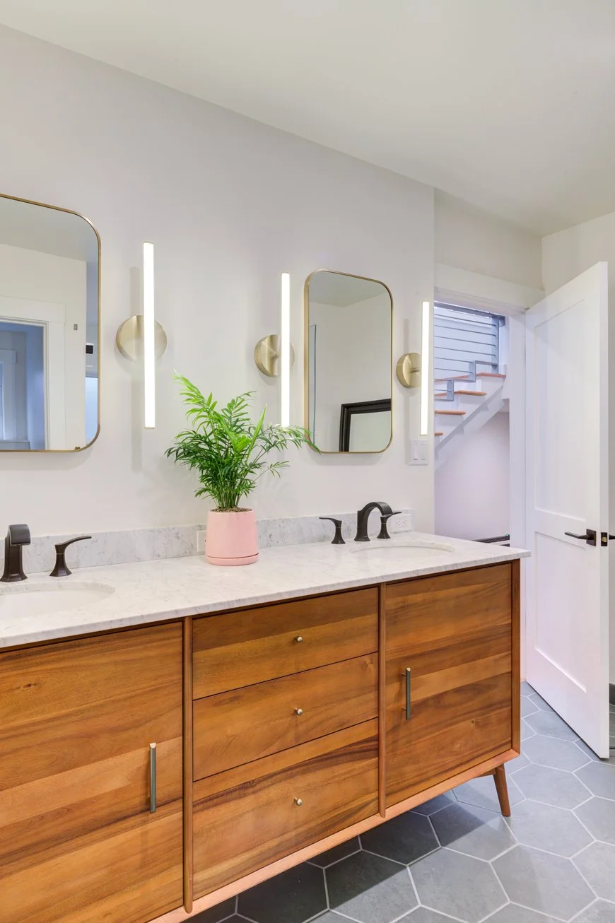 Primary bathroom vanity with warm walnut cabinetry, two sinks, marble countertop, and vertical wall sconces, designed to support shared use while bringing light and warmth into the space.