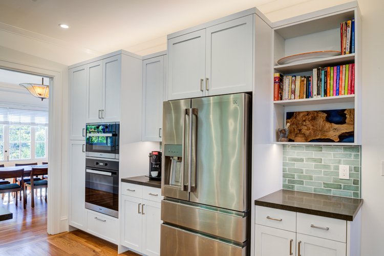 Tall cabinet wall with integrated refrigerator, ovens, and open display shelving, blending modern storage needs with materials and proportions respectful of the original Julia Morgan design.