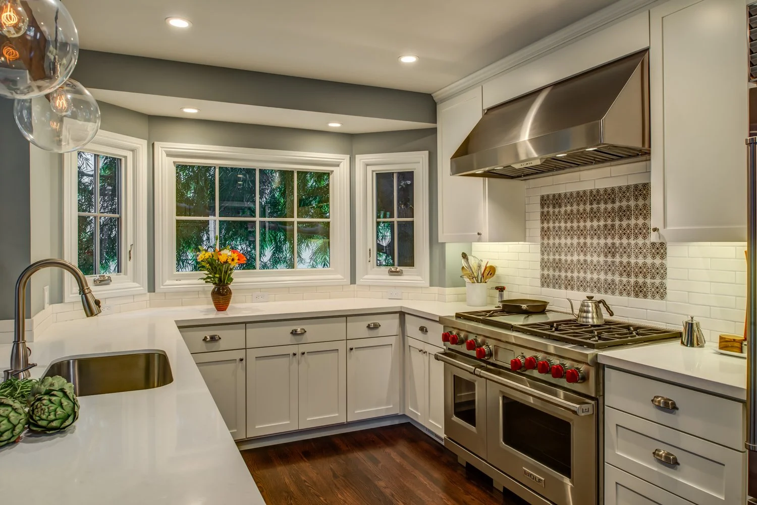 Light filled kitchen corner with wraparound counters, generous storage, a patterned backsplash behind the range, and multiple windows that make the space easier to navigate.