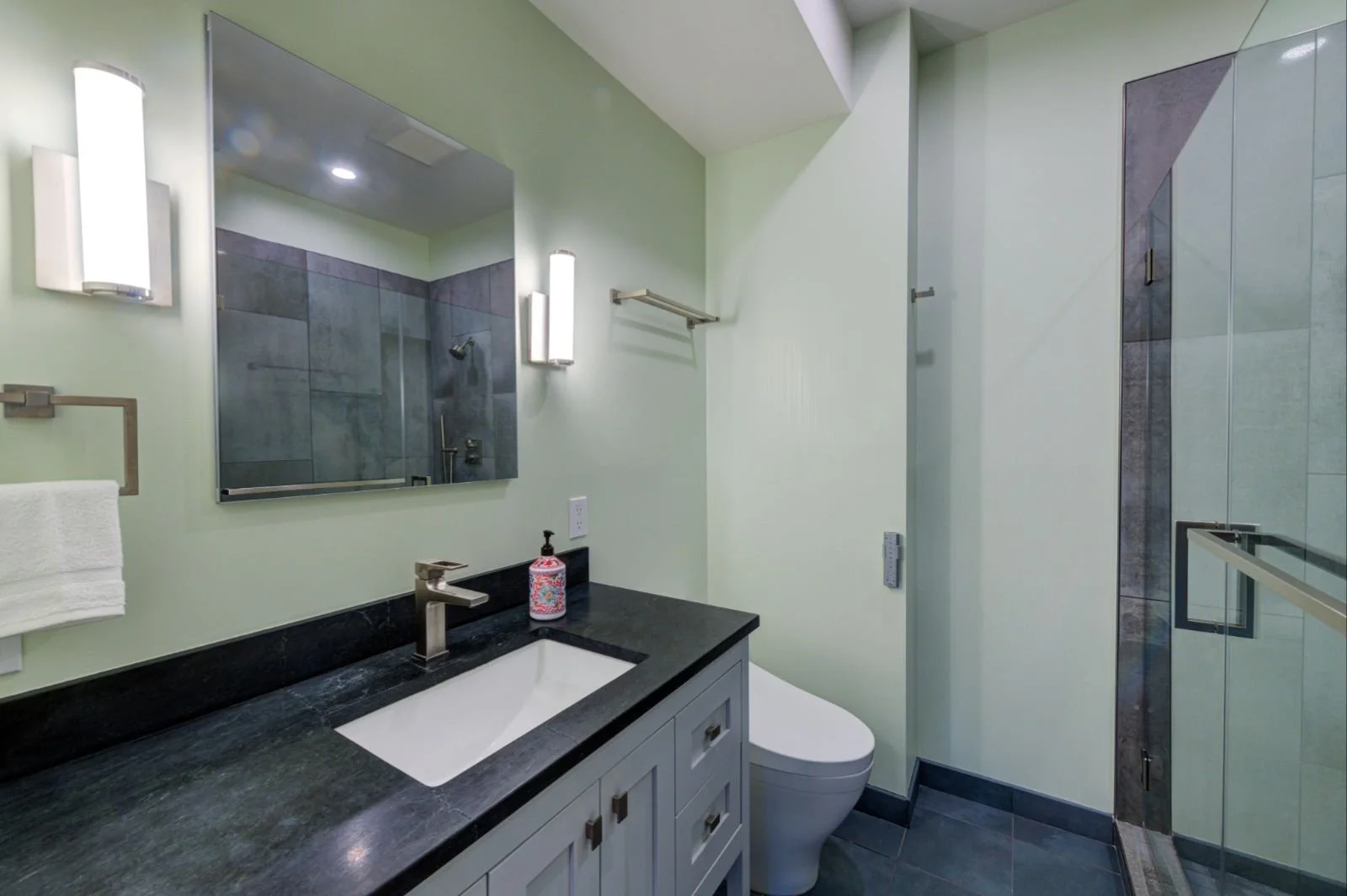 Compact bathroom in the Grand Lake ADU by Levitch with floating vanity, dark stone counter, modern mirror lighting, glass shower enclosure, and gray tile.