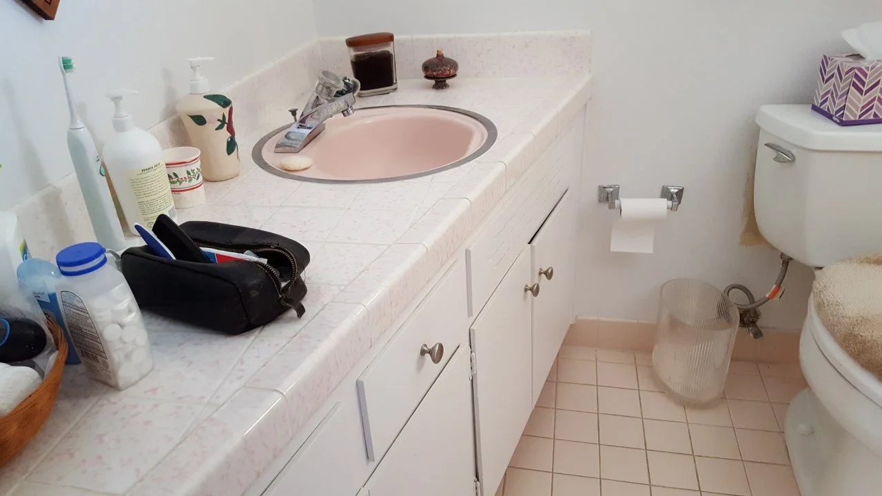 Original bathroom vanity with pink sink, laminate countertop, basic cabinetry, and outdated finishes that were replaced during the Alameda home renovation.