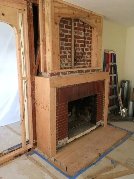 Construction phase view of the old wood burning fireplace with exposed framing and brick, prepared for a gas insert and a modernized mantel surround with niche.
