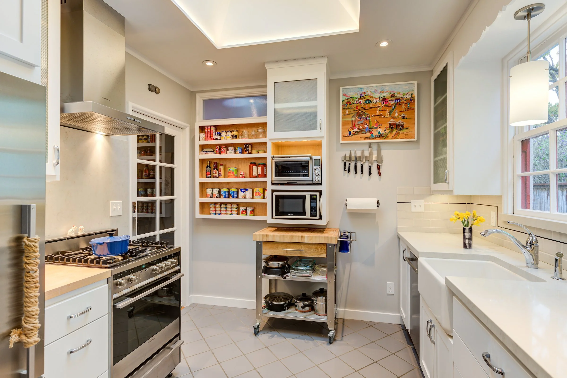 Overall view of Kitchen with fridge and range to the left, wall storage, and sink to the right.