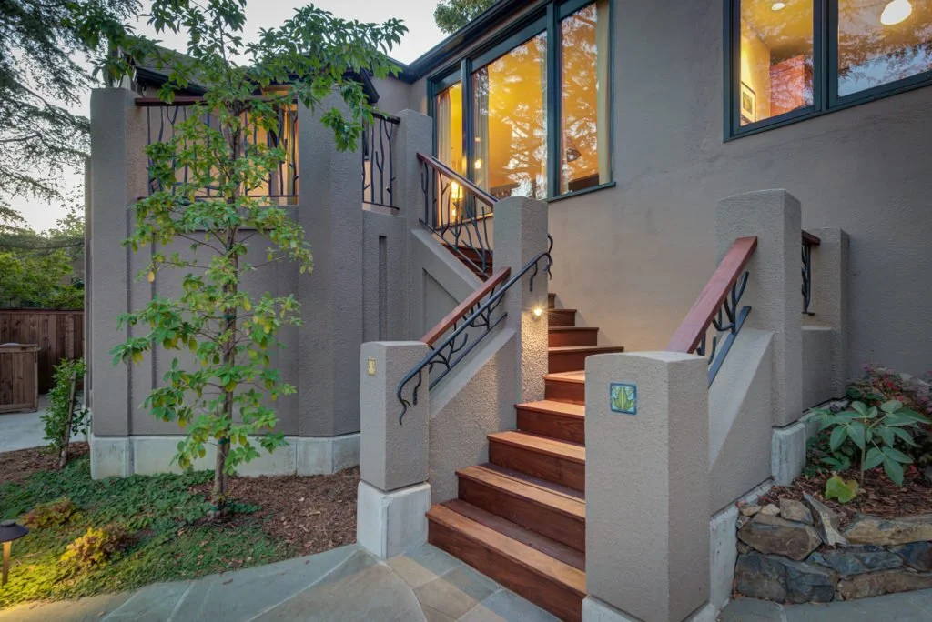 Closer view of the lower entry stairs with wood treads, stucco sidewalls, and nature inspired metal railing, replacing steep stairs with a safer and more welcoming path.