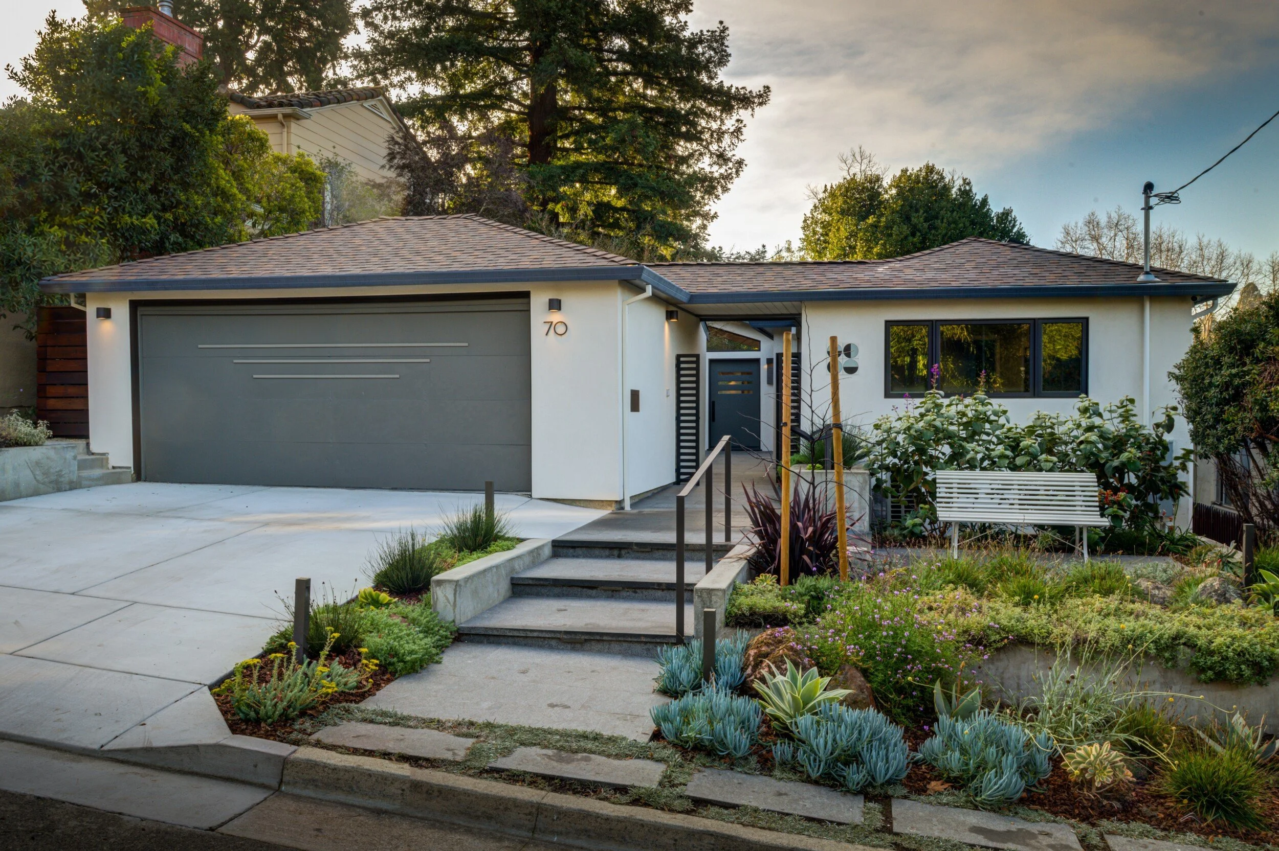 Front of home with new metal railings and gate along stepped walkway with new landscaping and a seating area in the front yard