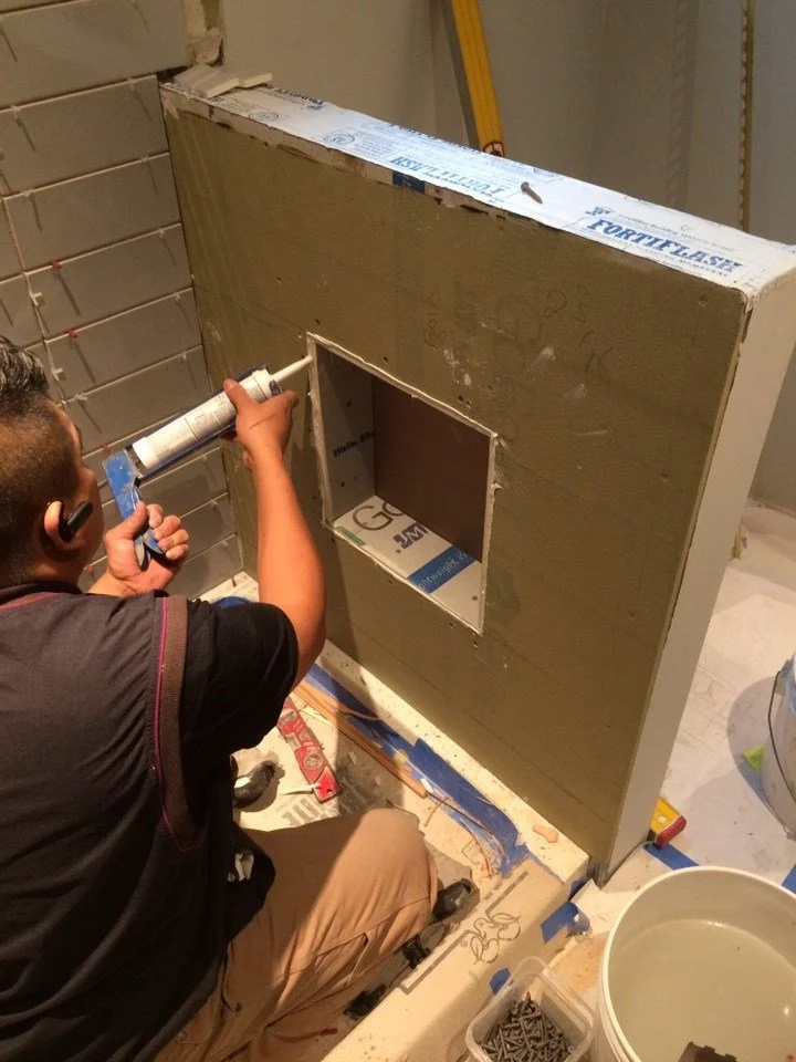 A contractor installs and waterproofs a recessed shower niche during bathroom construction for the Lighthearted Kitchen and Family Room Addition project.