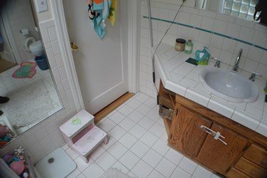 Original bathroom before renovation, showing an older vanity, tiled surfaces, and compact layout that was later redesigned.