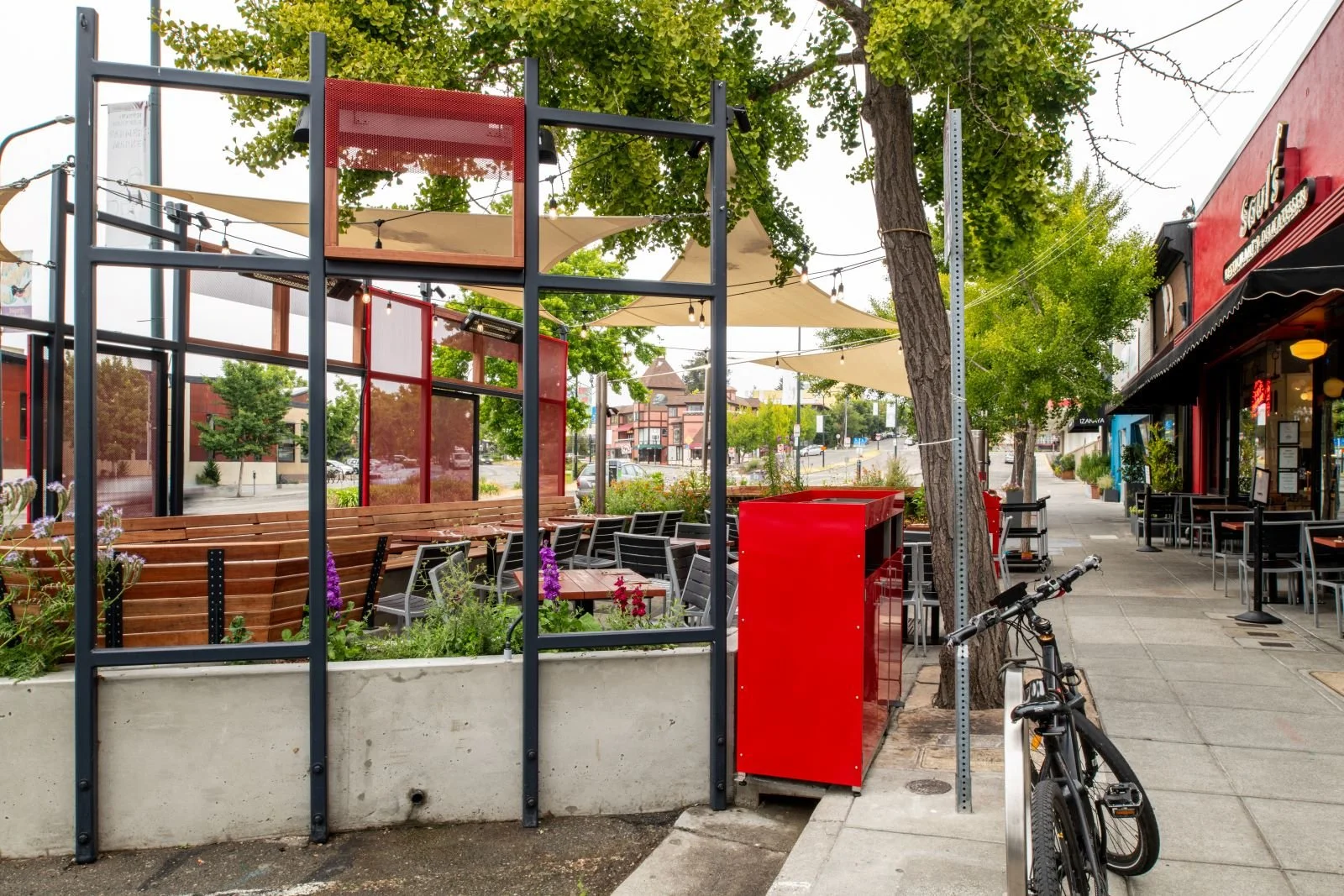 Side view of the structural aspects of the Parklet with steel frame elements. Planters with flowers lining the edges and existing street trees.