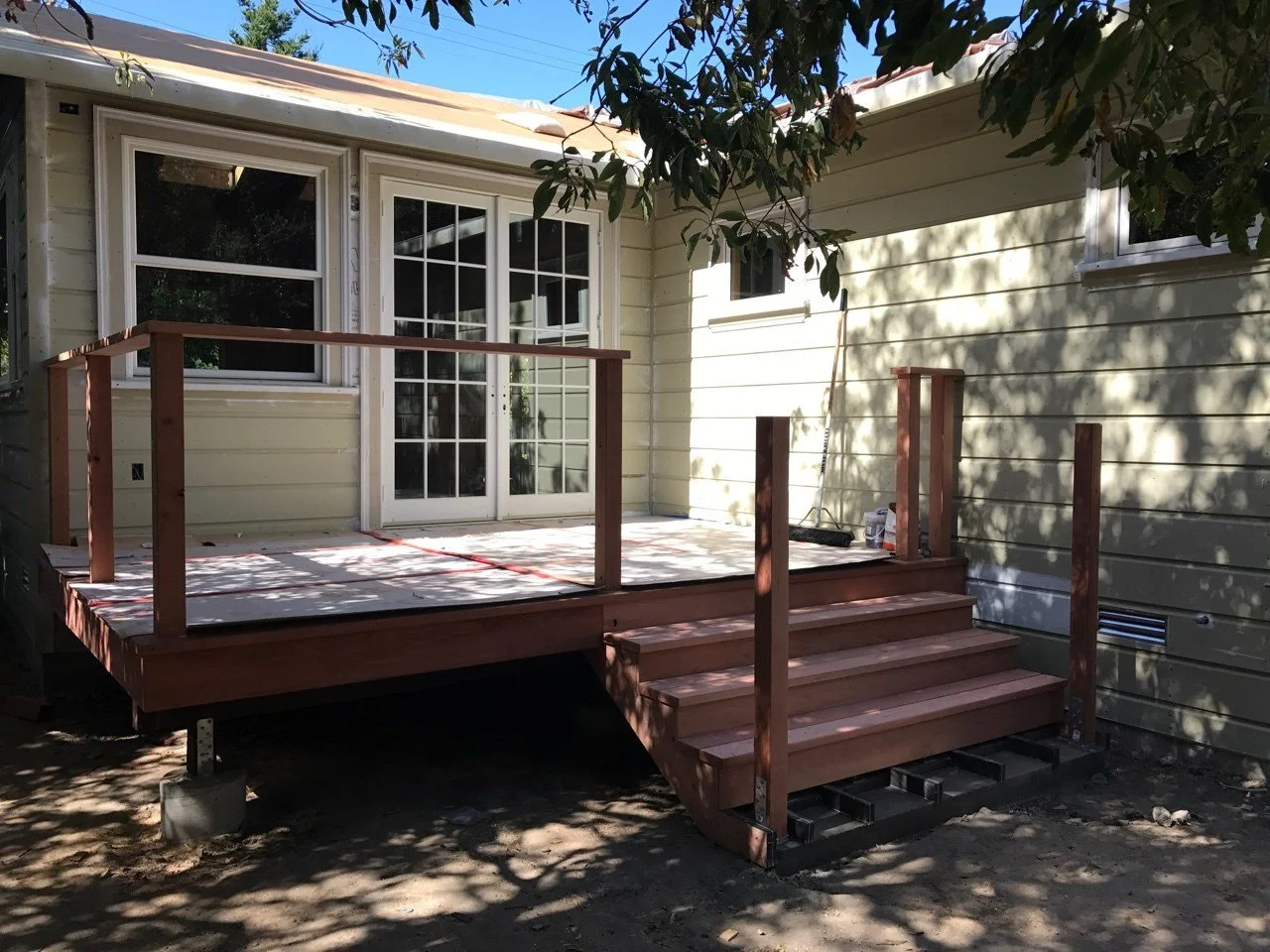 New rear deck under construction, showing framing, stairs, and railing posts being installed to create outdoor access from the home.