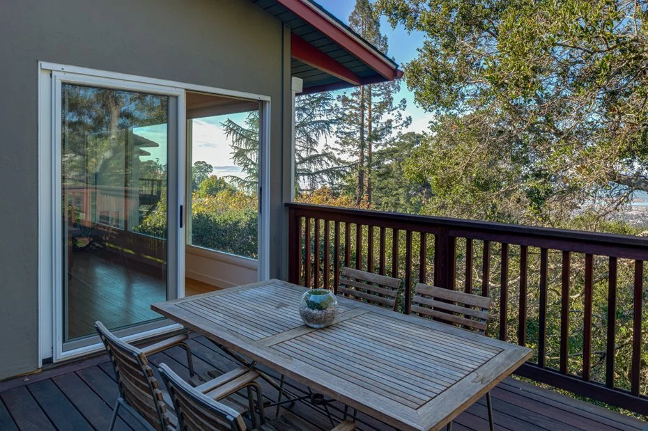 Outdoor deck accessible from the living area, furnished with a dining table and surrounded by mature trees.
