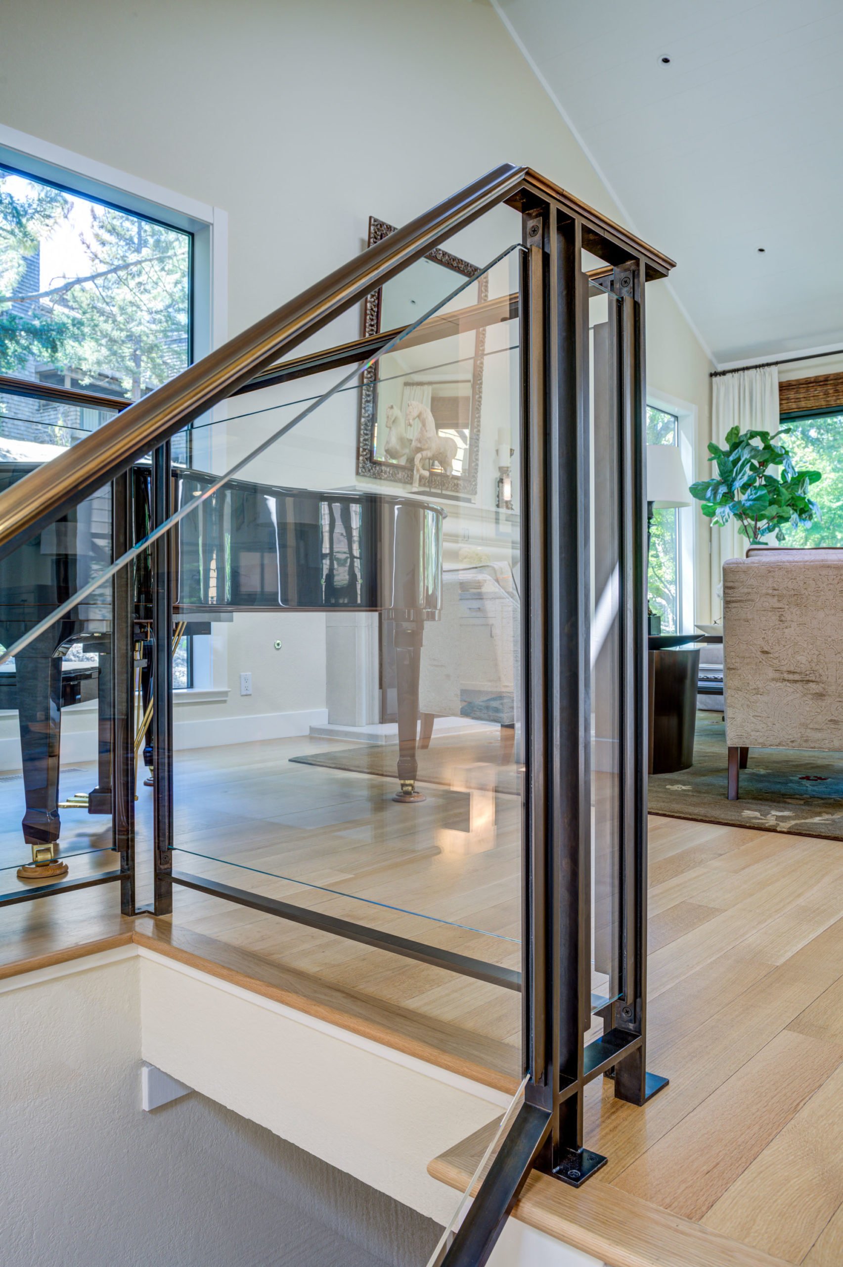 Close-up of the custom glass and metal stair railing designed by Levitch, highlighting clean lines, transparency, and integration with the refinished wood floors.