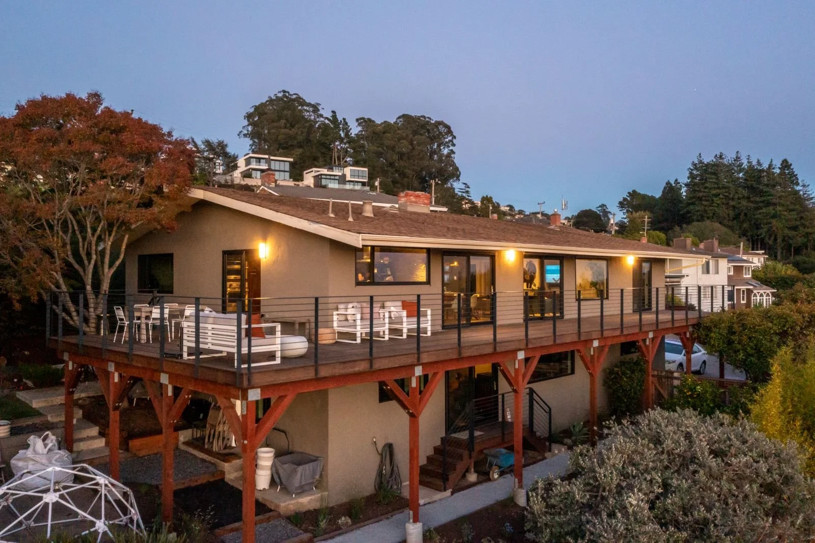 A wide exterior view reveals the new deck wrapping around two sides of the home supported on timber posts. The deck complements the home’s horizontal form and anchors it to the sloping site. It also connects all major rooms to the outdoors.