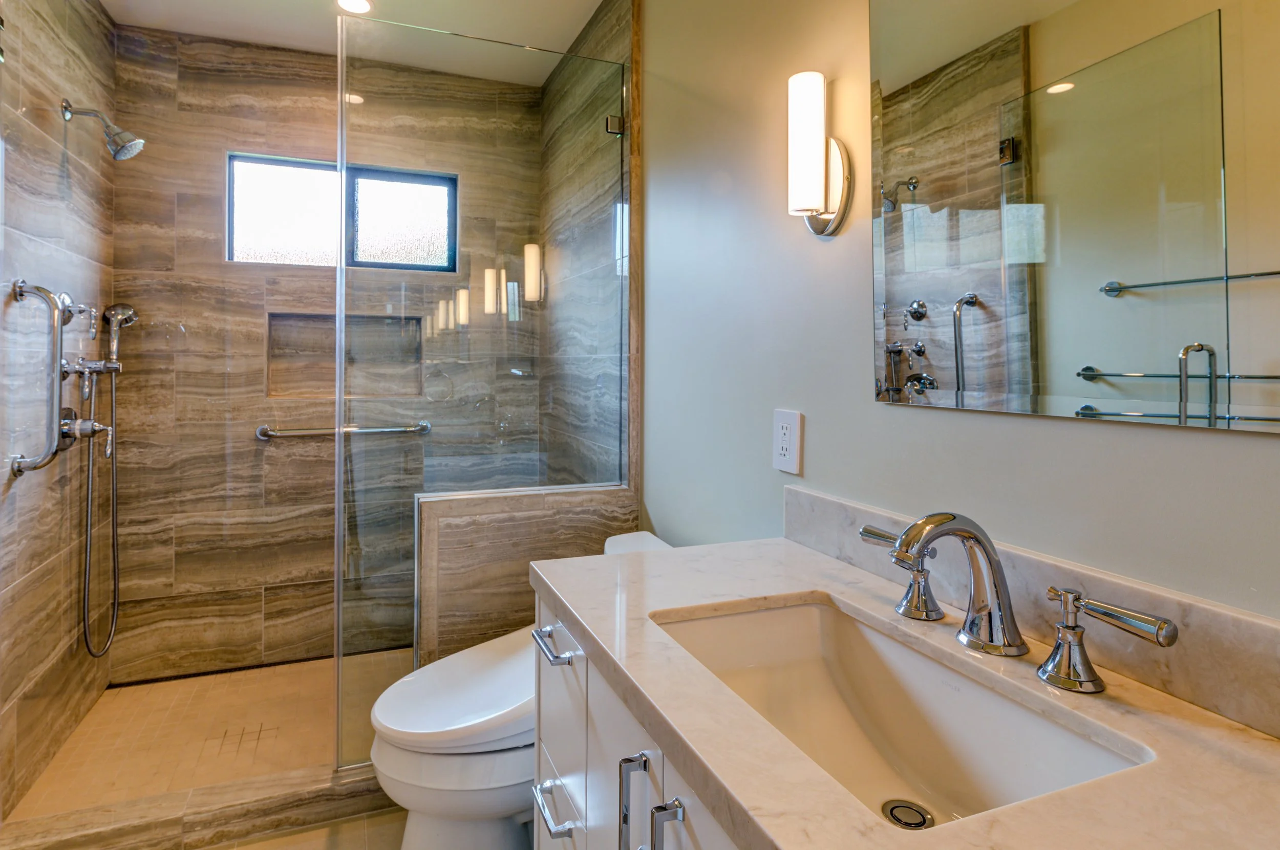 Residential bathroom featuring a walk in shower with clear glass enclosure, stone tile walls, built in niche, and a streamlined vanity designed for comfort and long term use.