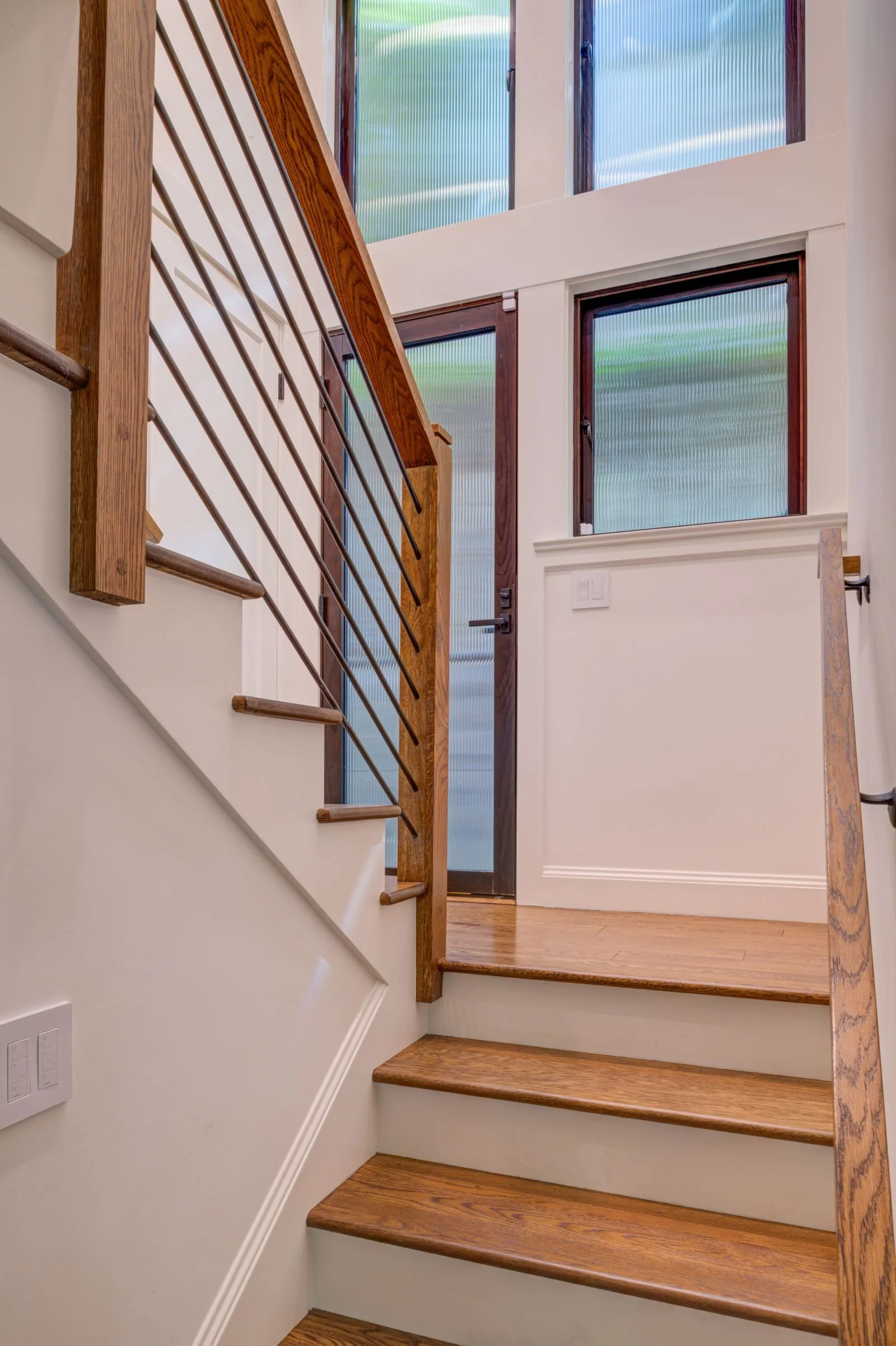 New Staircase to the Lower Level capturing the landing and tall translucent windows to match the door that provides access to the side yard. Hardwood flooring and stair treads with painted risers and metal rod and wood railing.
