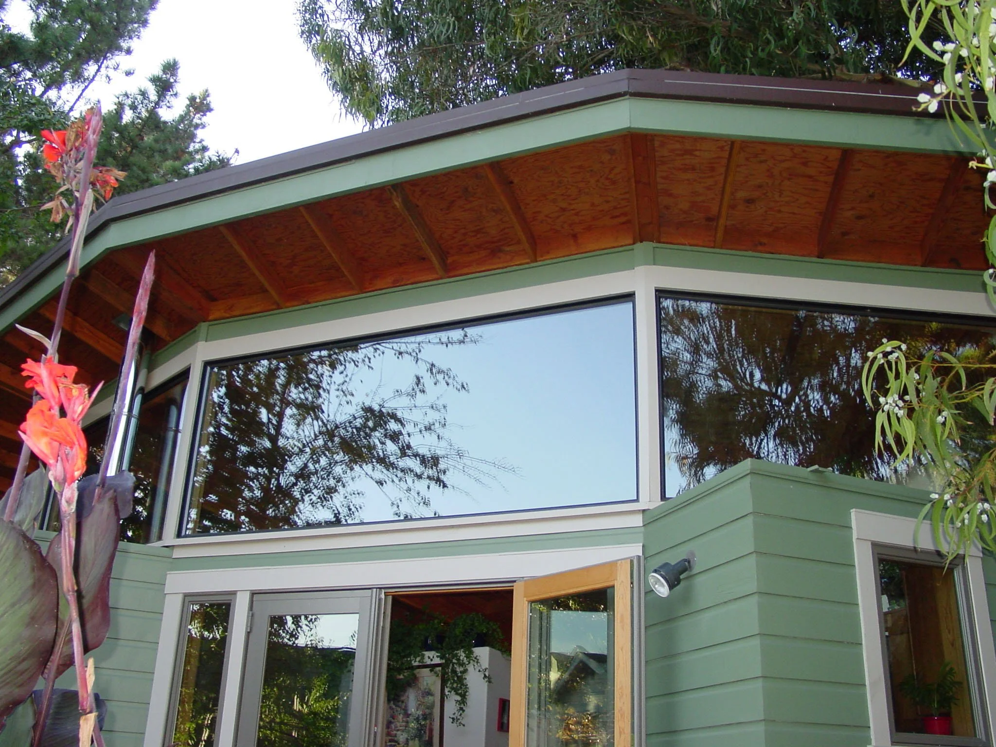 Corner view of the cottage roof and clerestory windows with deep eaves and wood soffits, bringing daylight into the small home while maintaining privacy from the surrounding garden.