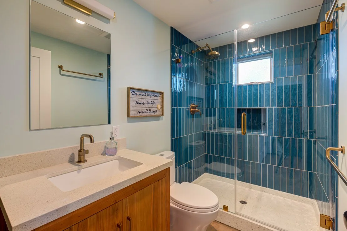 ADU Bathroom featuring a shower with vertically installed rectangular turquoise blue tile, a window and niche in this fully-sized and functional space.